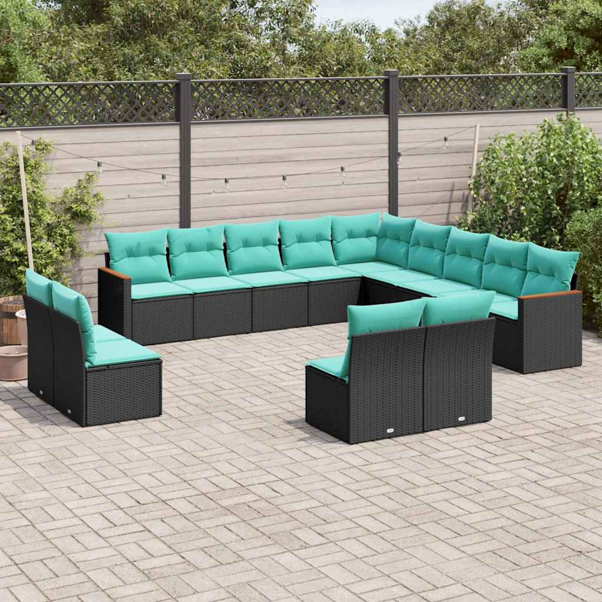 Eine U-förmige Gartenlounge aus schwarzem Rattangeflecht mit türkisfarbenen Kissen auf einer Kopfsteinpflasterterrasse.