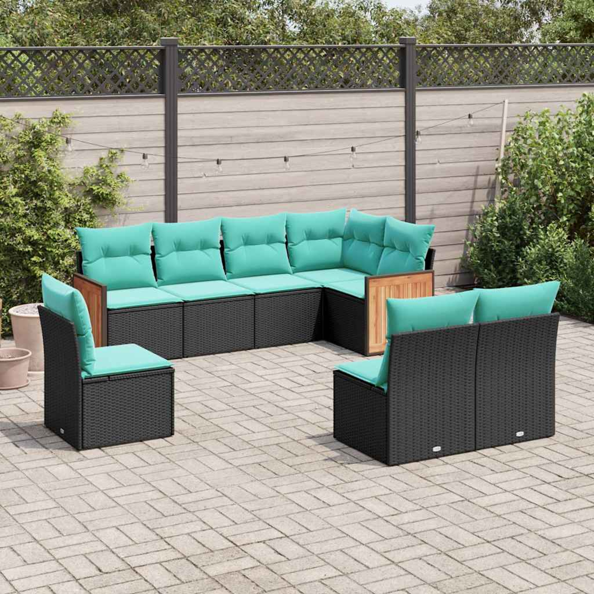 Ein modulares Outdoor-Sofa mit schwarzen Rattan-Elementen und türkisen Kissen auf einer Pflasterterrasse.