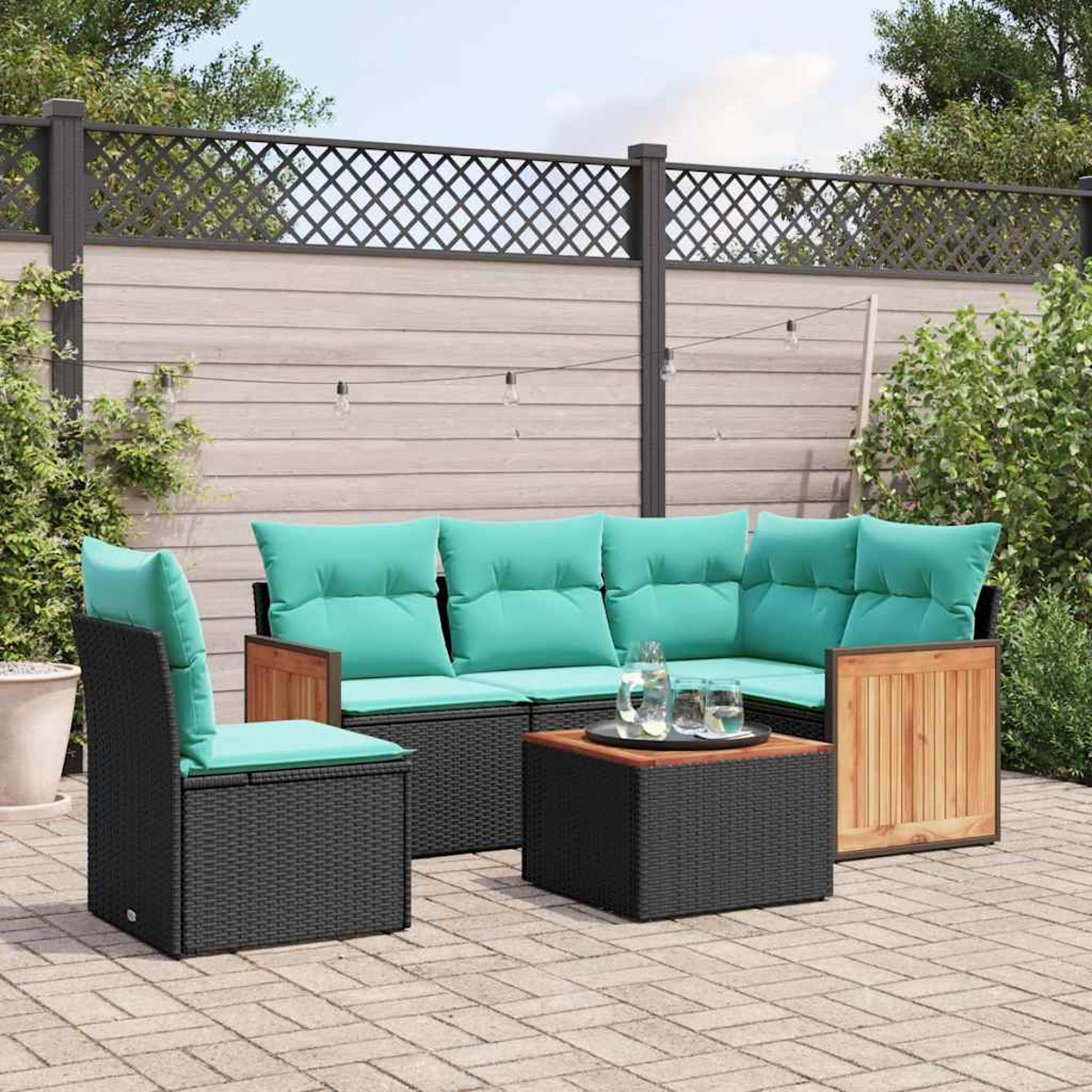 Gartenlounge mit schwarzen Rattansofas und türkisen Kissen, Couchtisch, auf Steinfliesen.