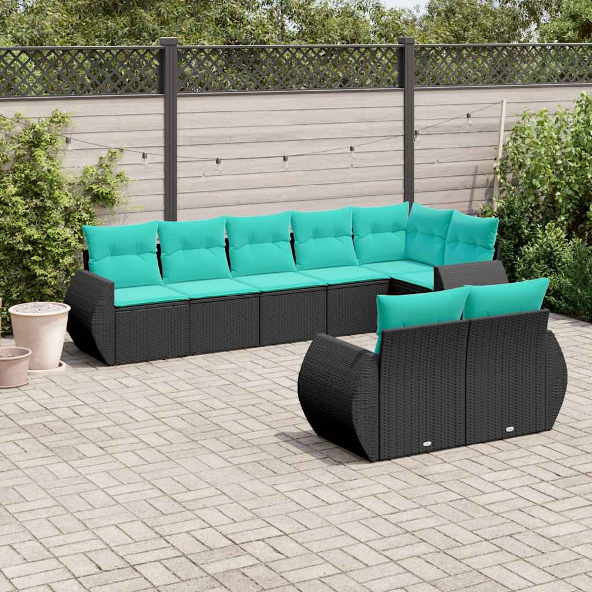Ein dunkles Rattan-Sofaset mit türkisfarbenen Kissen auf einer gepflasterten Terrasse.
