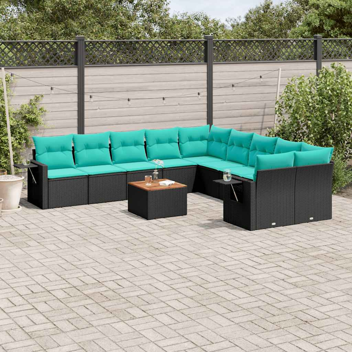 Ein schwarzes modulares Outdoor-Sofa mit türkisfarbenen Kissen steht auf einer gepflasterten Terrasse.
