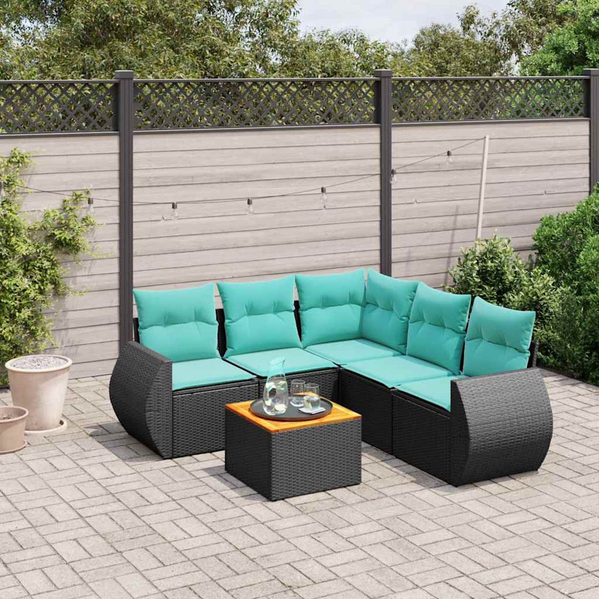 Ein schwarzes Rattansofa mit türkisen Kissen und ein Tisch stehen auf einer Steinterrasse.