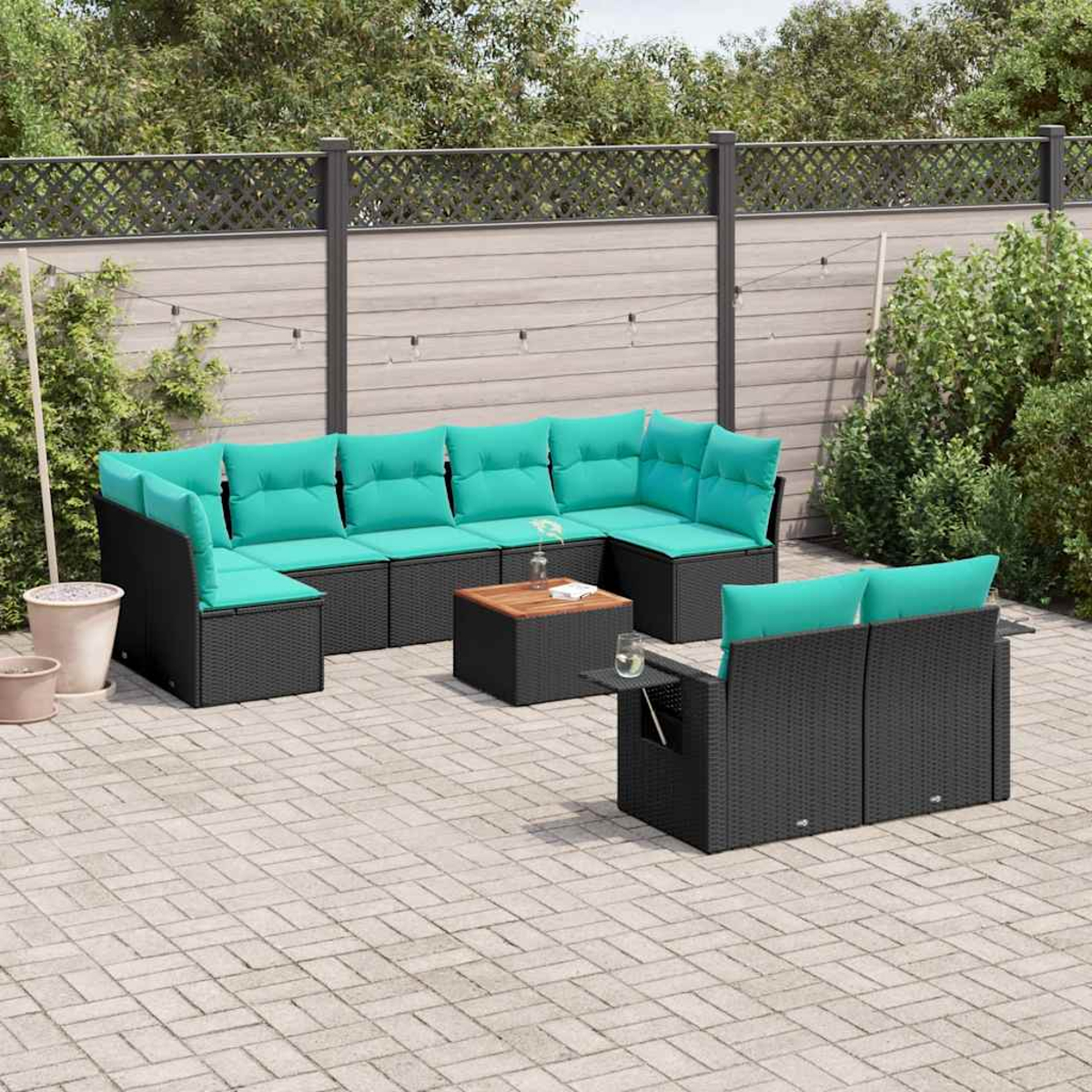Ein schwarzes Rattan-Sofa mit türkisen Kissen auf einer gepflasterten Terrasse.