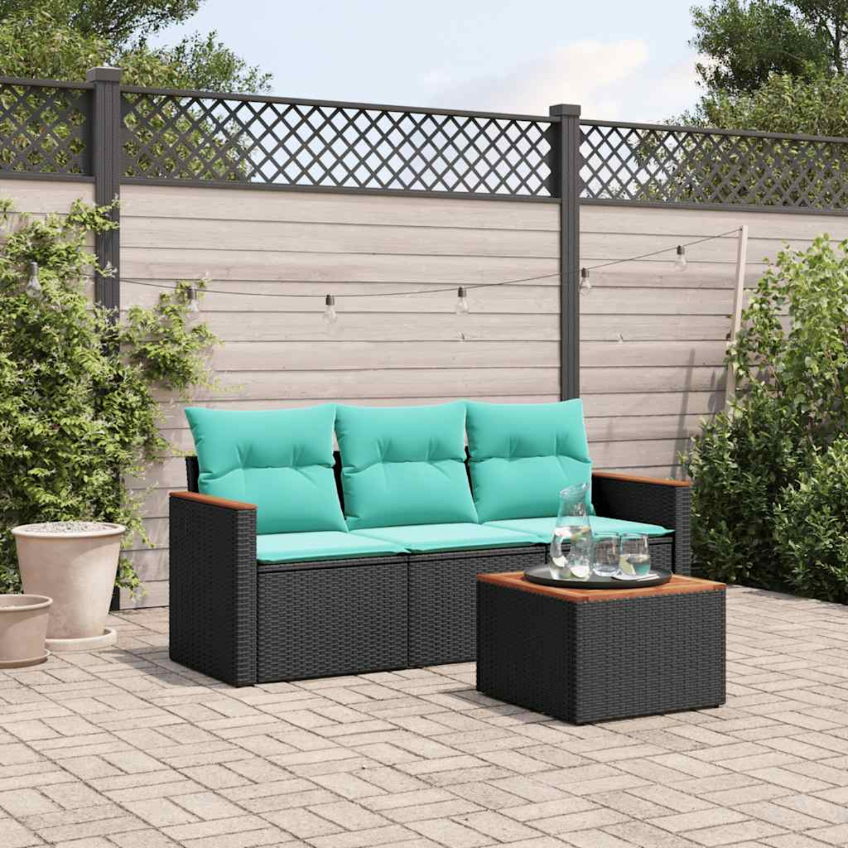 Ein dunkles Rattan-Sofa mit türkisfarbenen Kissen und ein passender Tisch im Freien.