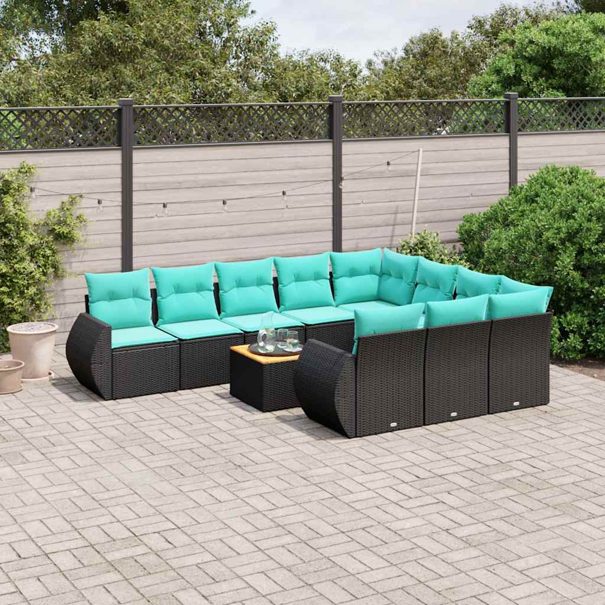 Eine dunkle Rattansofa-Garnitur mit türkisfarbenen Kissen auf einer gepflasterten Terrasse.