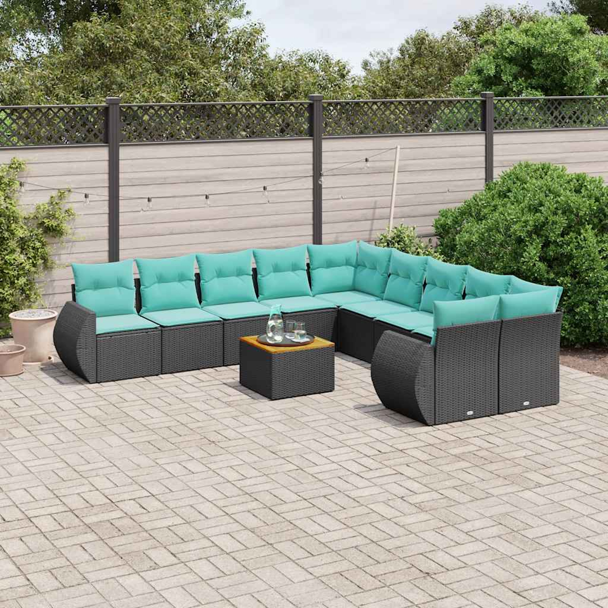 Ein graues Lounge-Set mit türkisen Kissen steht auf einer gepflasterten Terrasse.