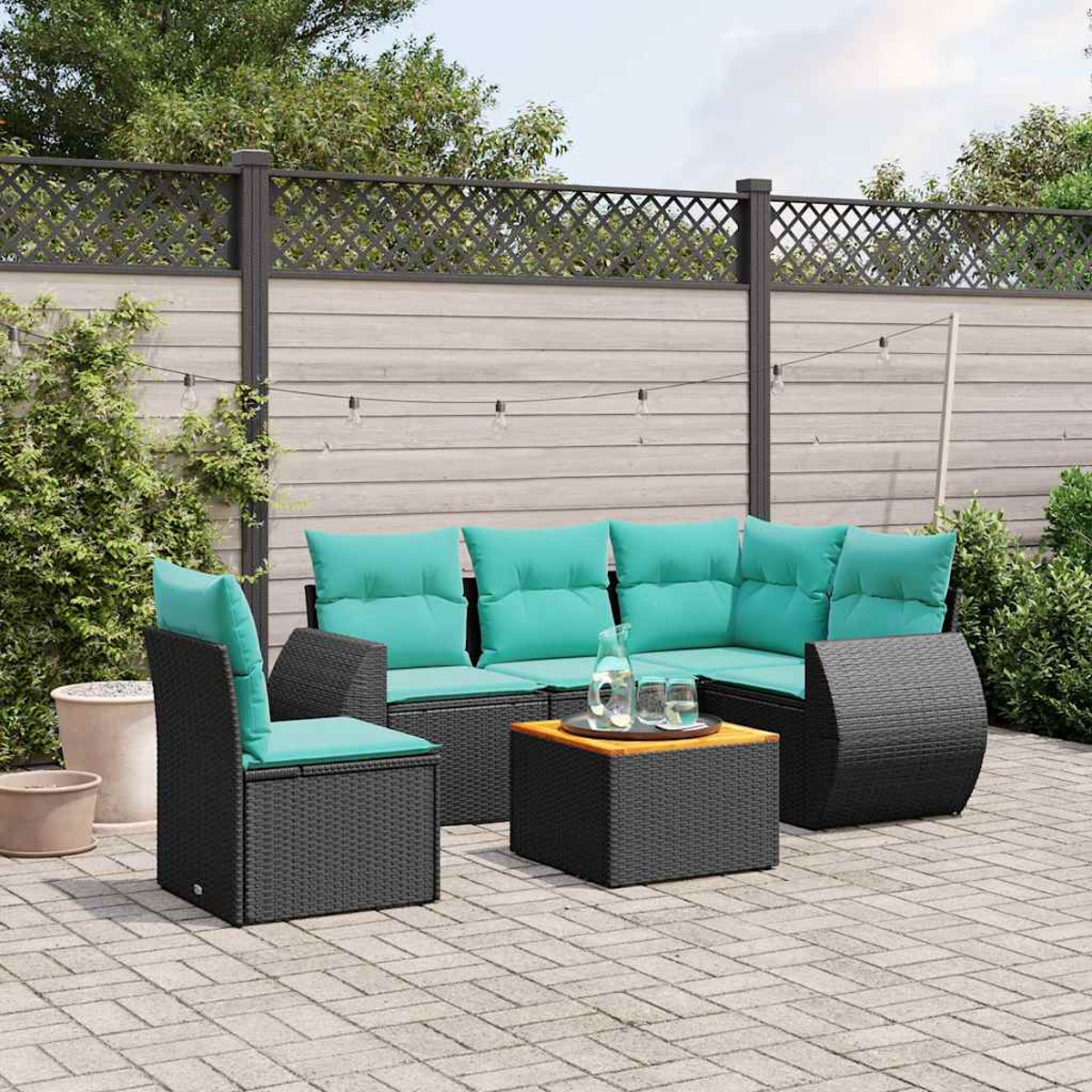 Dunkelgraue Rattan-Gartenmöbel mit türkisfarbenen Kissen auf einer gepflasterten Terrasse.