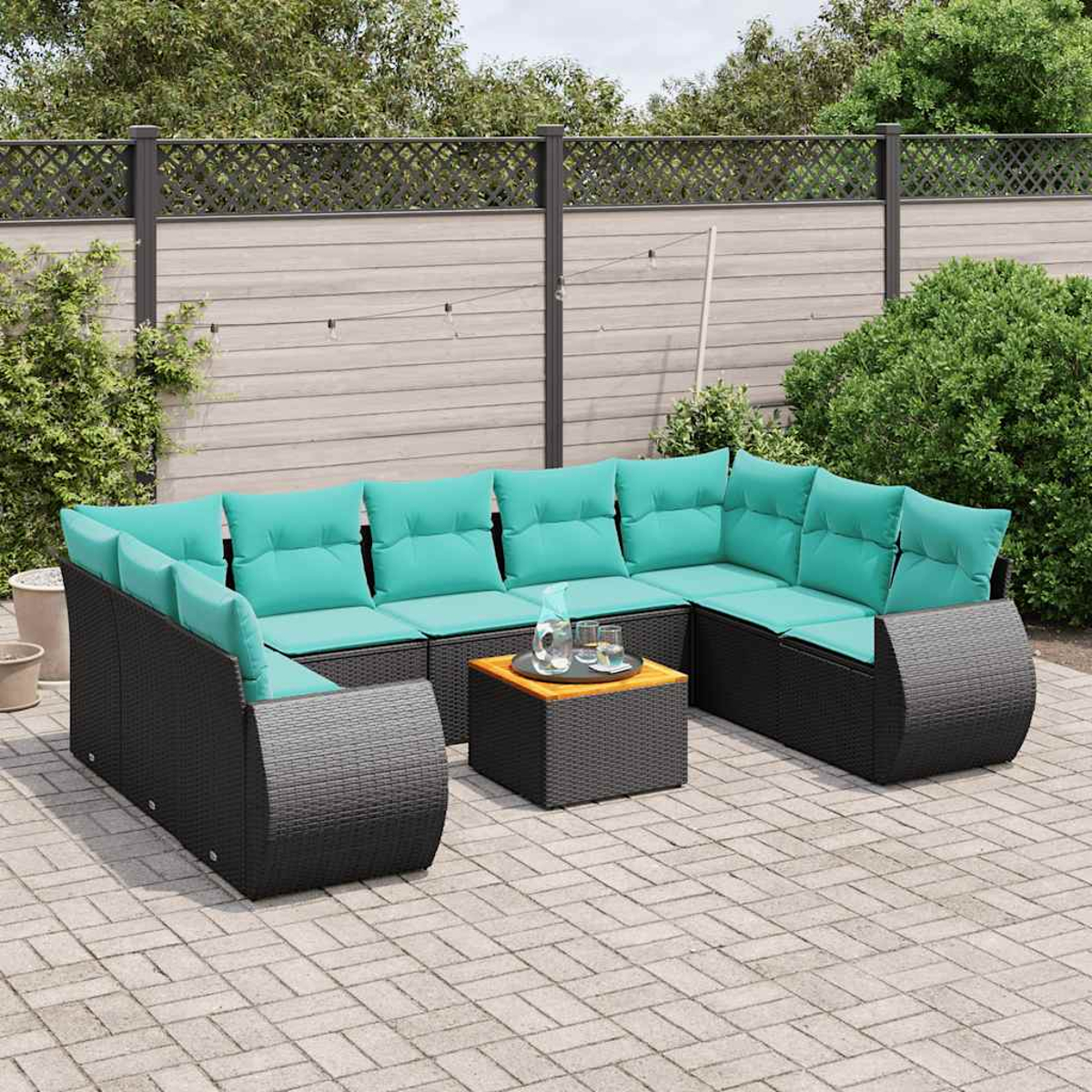 Ein schwarzes Rattan-Sofa mit türkisfarbenen Kissen steht auf einer Terrasse.