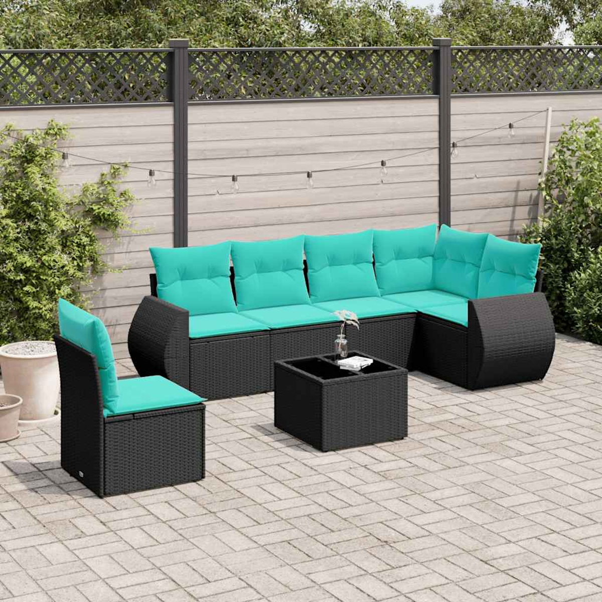 Ein schwarzes Rattansofa mit türkisfarbenen Kissen und ein passender Stuhl auf einer Terrasse.