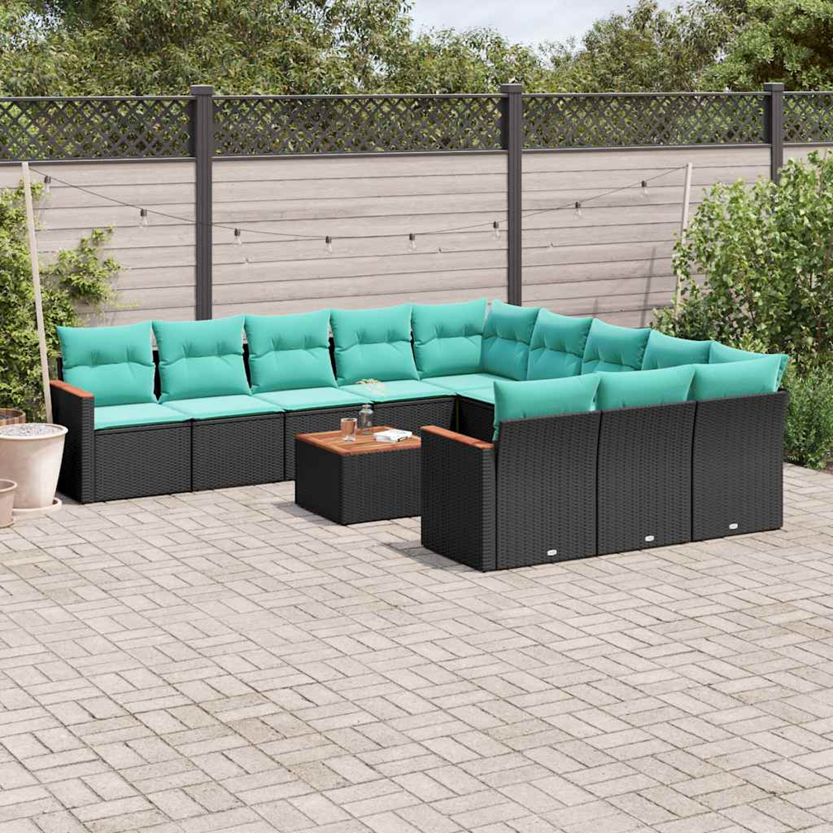 Ein schwarzes Rattan-Ecksofa mit türkisfarbenen Kissen auf einer gepflasterten Terrasse.