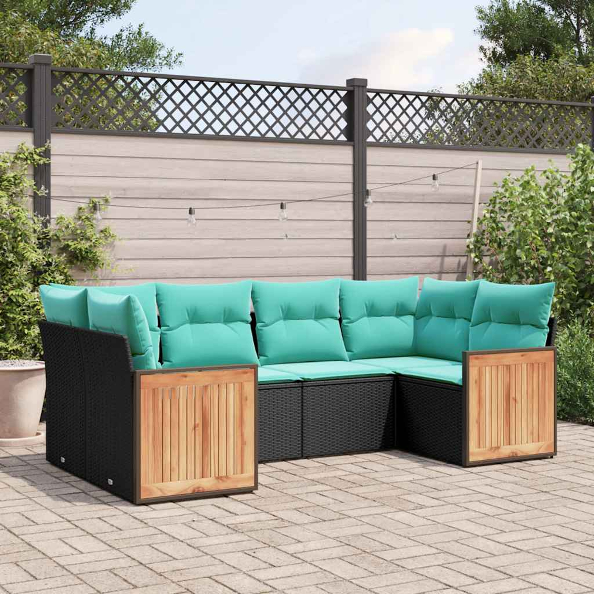 Ecksofa aus schwarzem Rattangeflecht mit hellgrünen Kissen und Holzakzenten auf einer Terrasse.