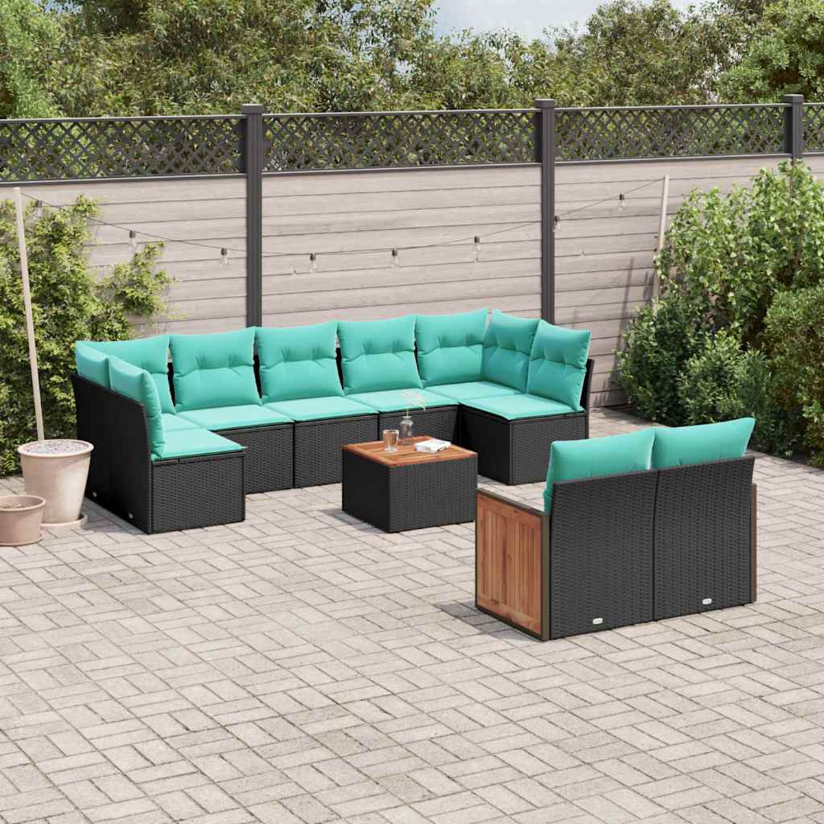 Gartenlounge mit schwarzen Rattan-Möbeln und türkisen Polstern auf einem Steinpflaster.