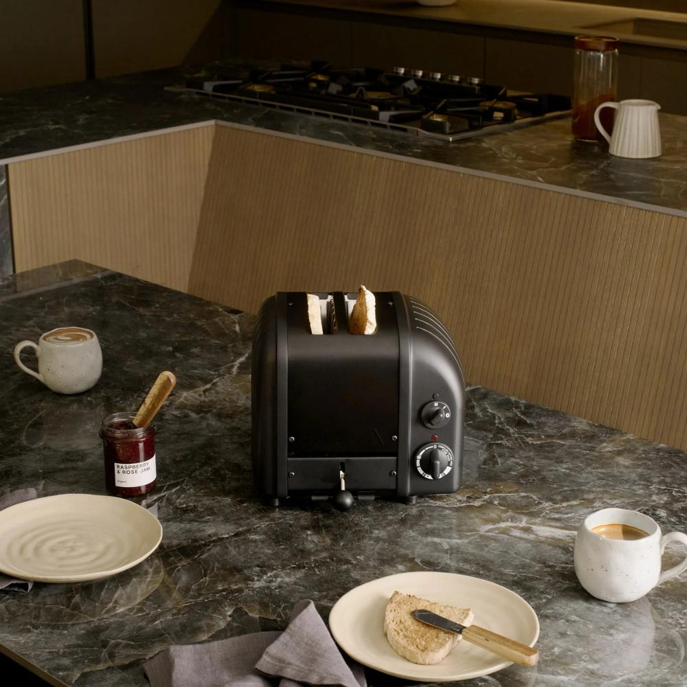 Schwarzer Toaster mit Toast, Marmelade, Kaffee und Toast auf einem Marmortisch.