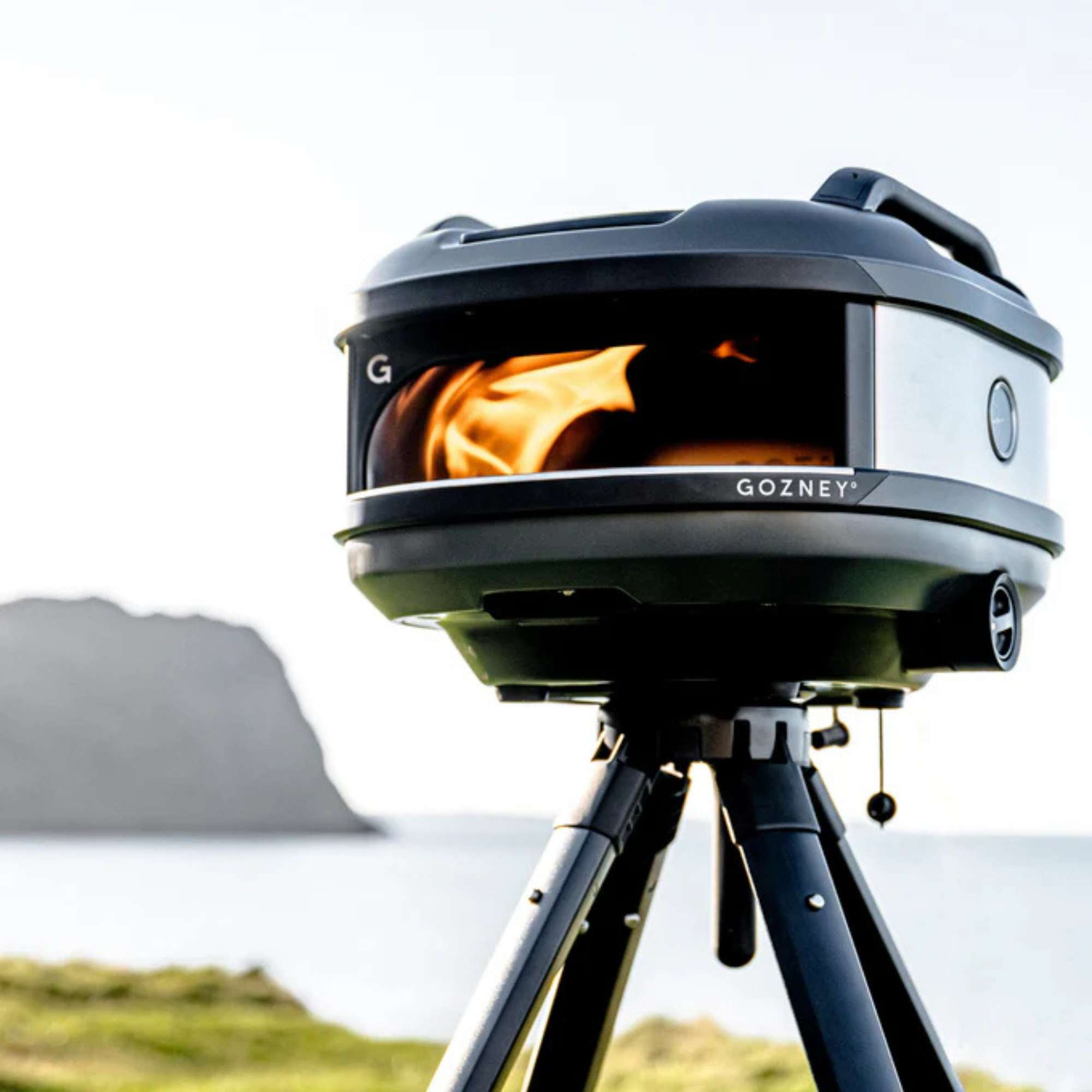 Ein Gozney Pizzaofen mit Flammen auf einem Stativ am Meer.