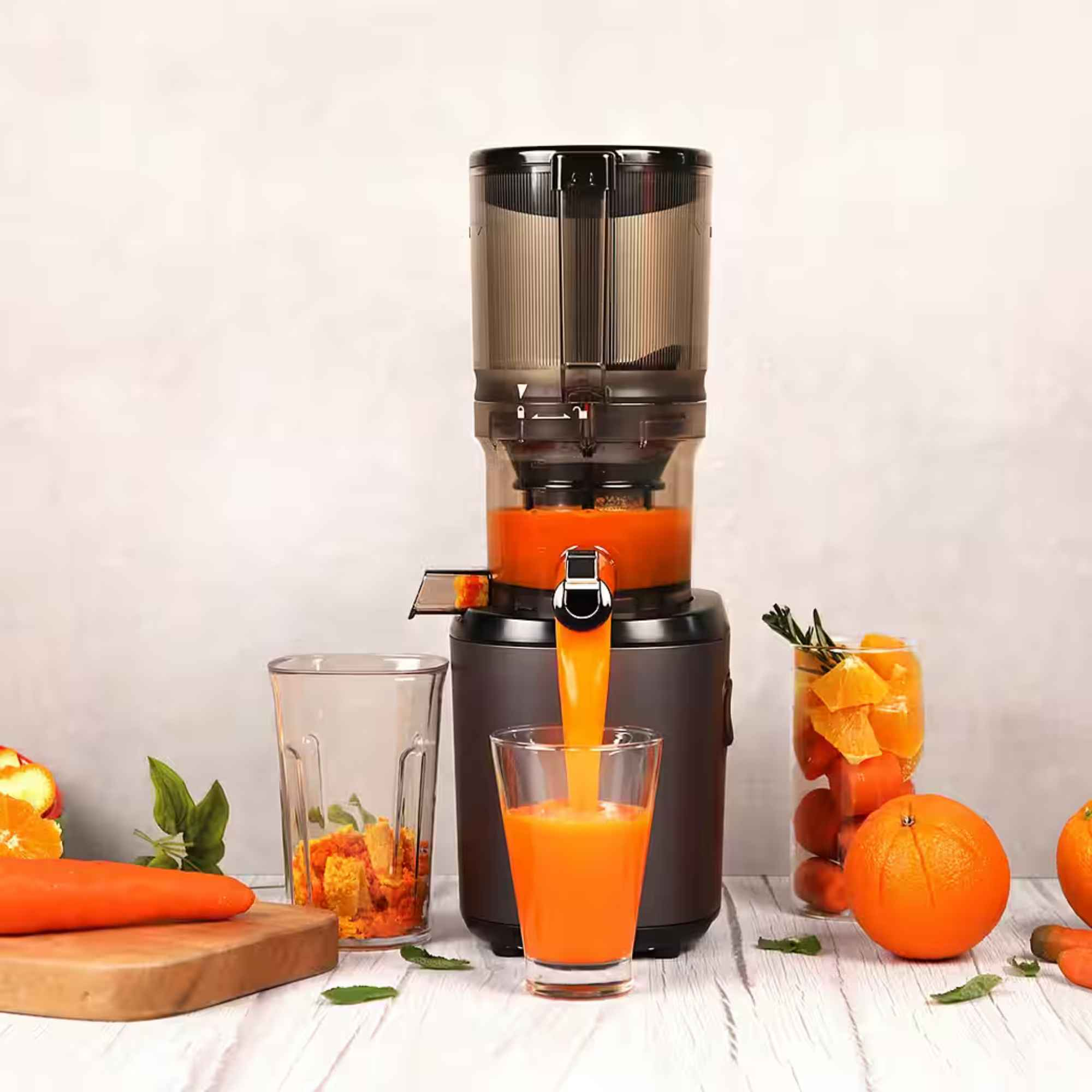 Ein Entsafter presst Orangensaft in ein Glas. Daneben liegen Orangen und Karotten.
