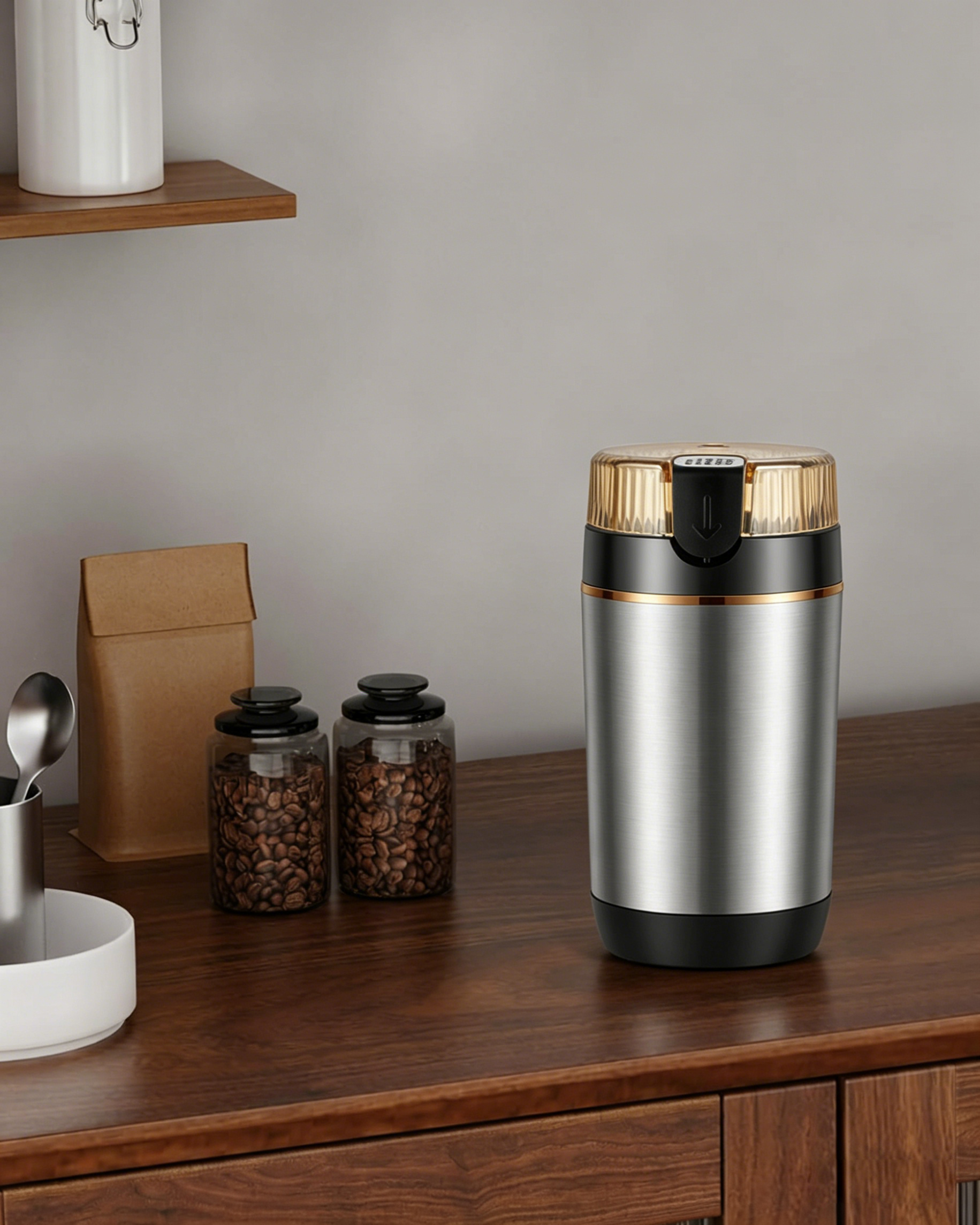 Kaffeemühle aus Edelstahl mit goldenem Deckel und zwei Gläsern Kaffeebohnen.