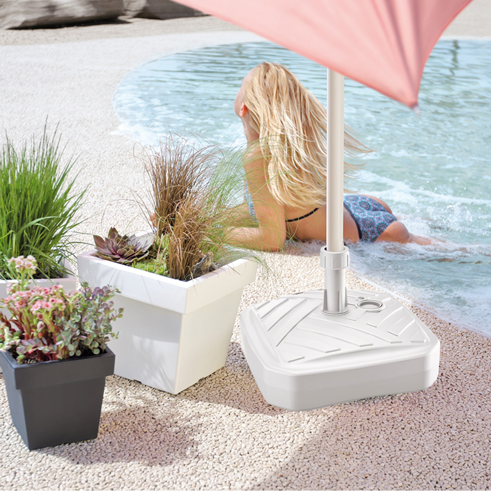 Una mujer rubia yace junto a una piscina con sombrilla y plantas en primer plano.