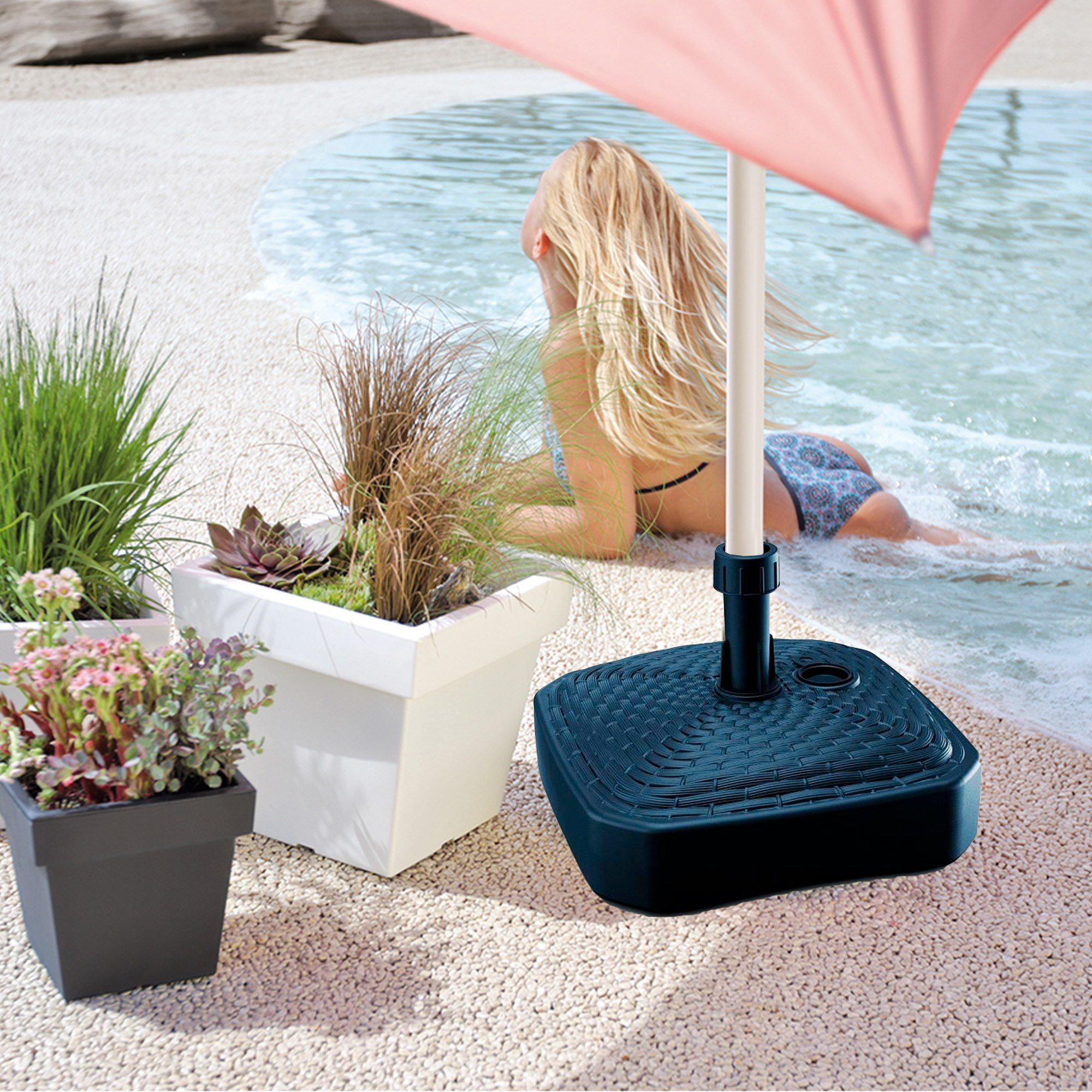 Mujer en bikini yace en la playa, soporte de sombrilla y plantas delante.