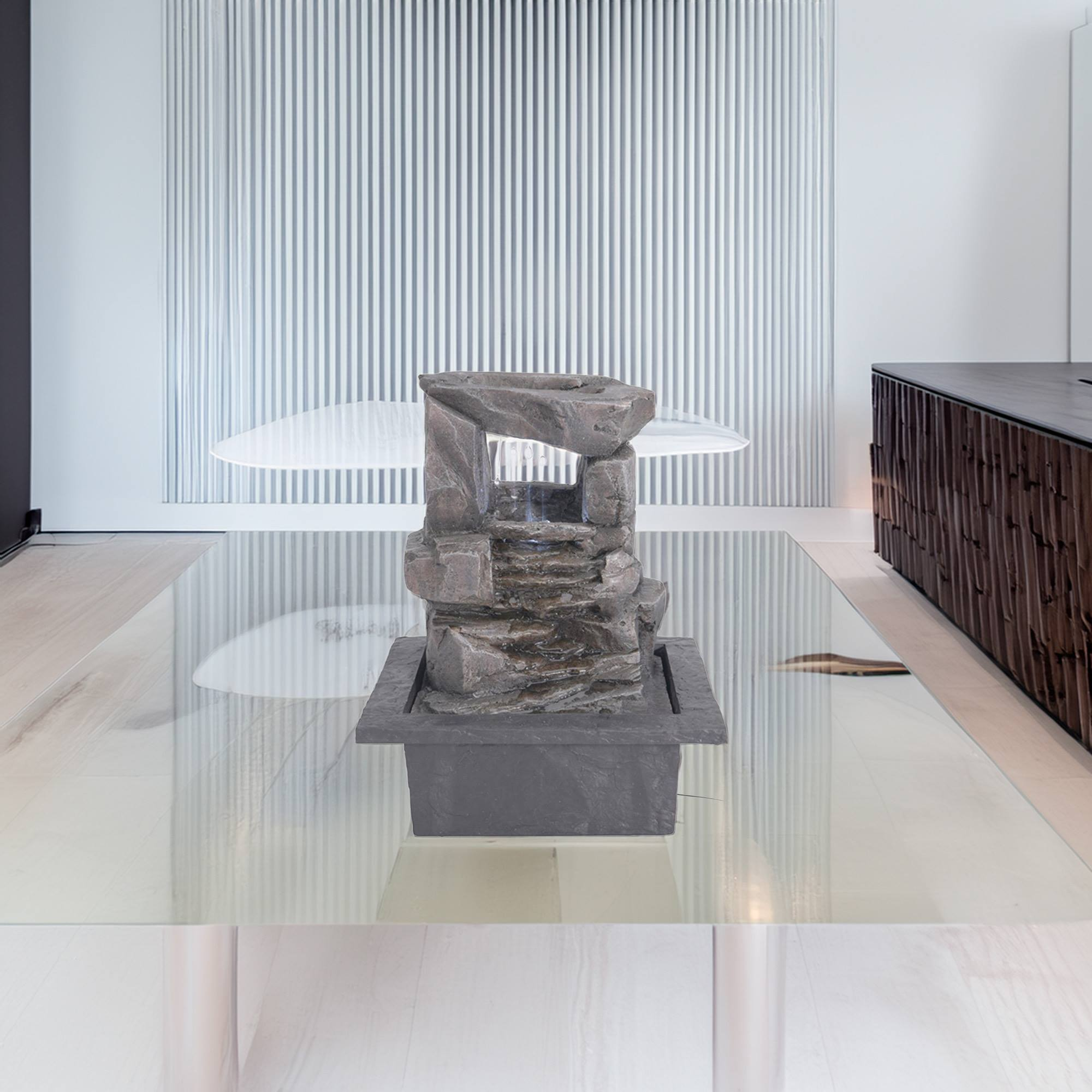 Una pequeña fuente de piedra sobre una mesa de cristal frente a una pared vertical.