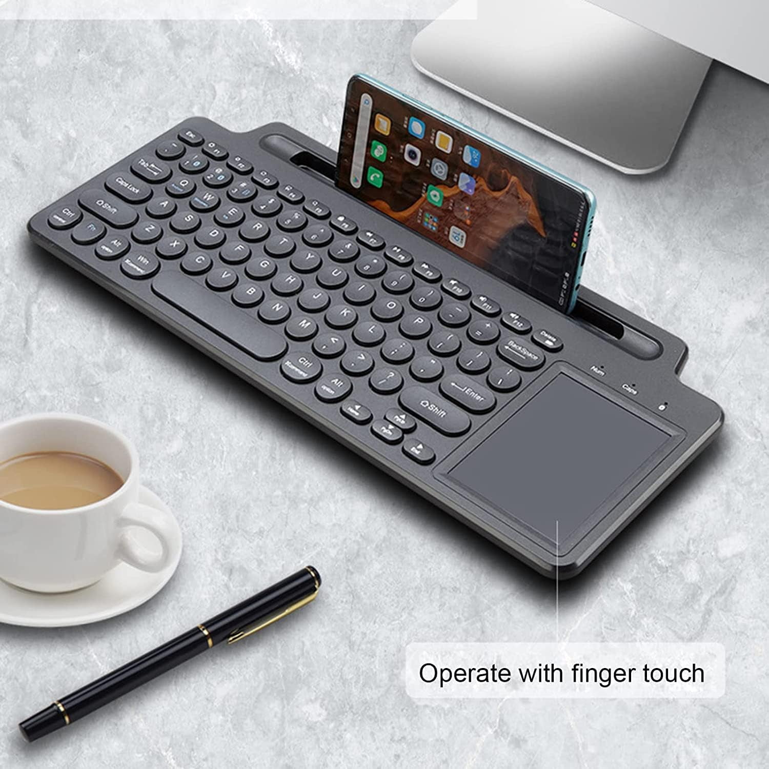 Graue Tastatur mit Smartphone-Halterung, Tasse Kaffee und Stift.