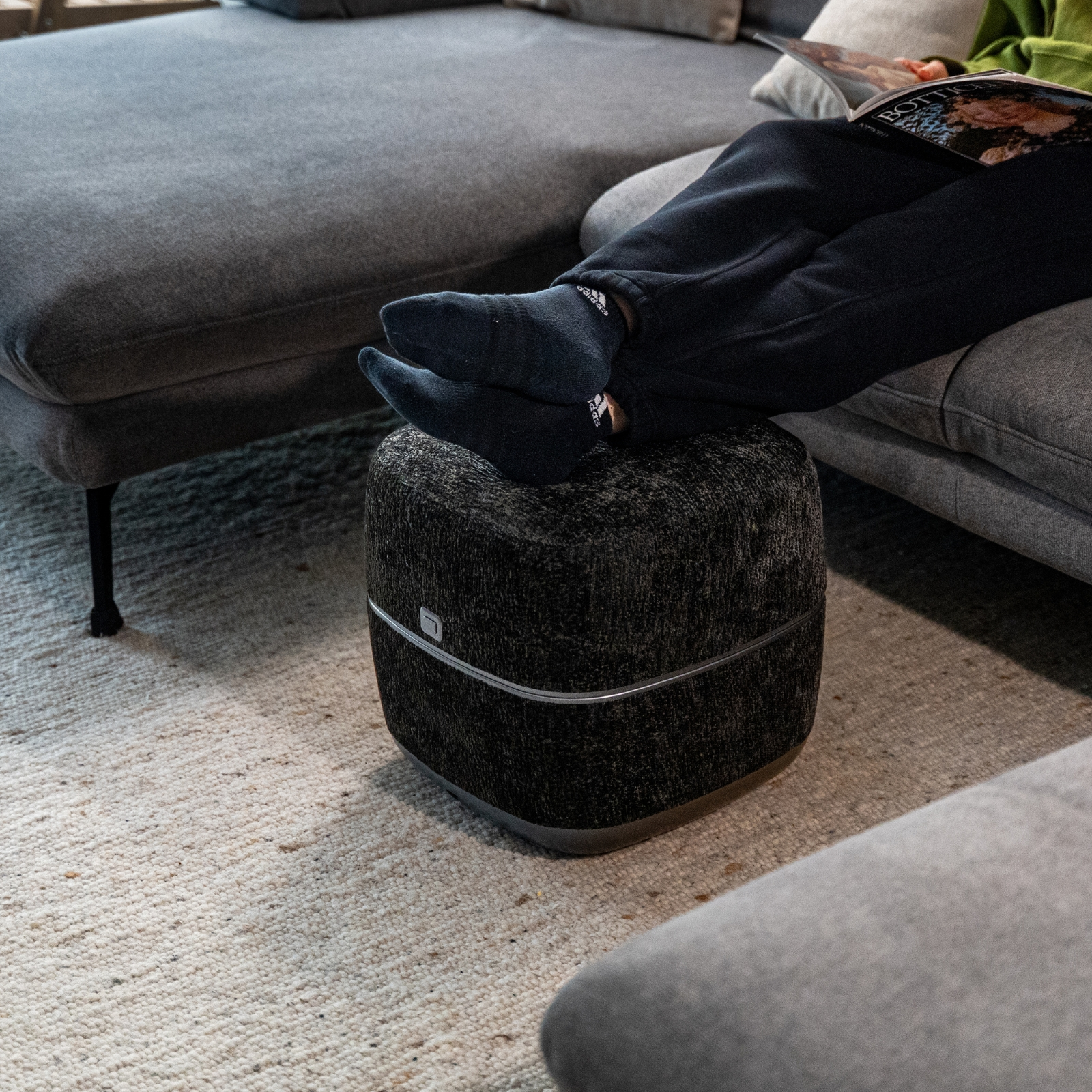 Eine Person mit dunklen Socken liegt auf einem Sofa und liest ein Magazin.