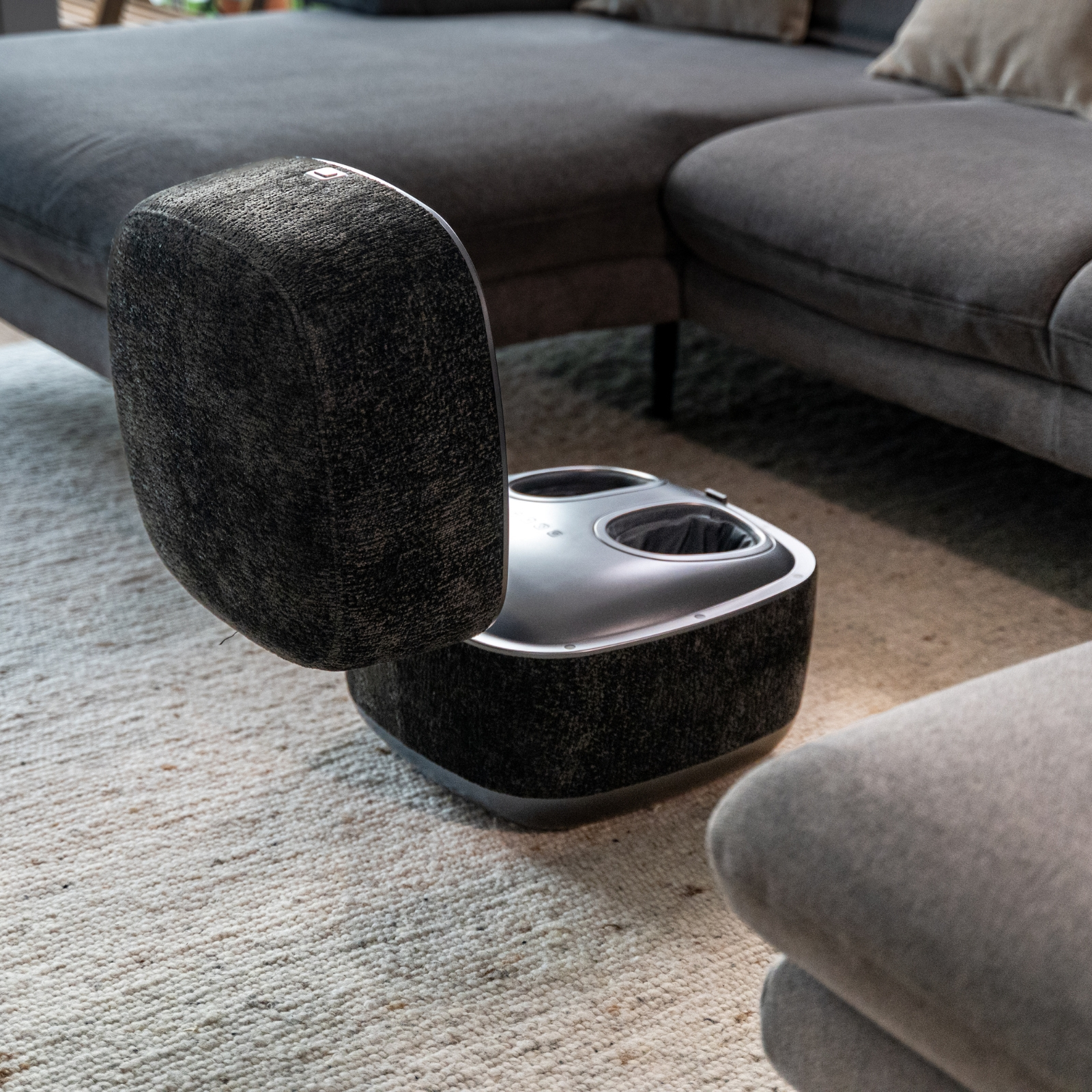 Ein schwarzer Fußmassagegerät steht auf einem Teppich neben einem Sofa.