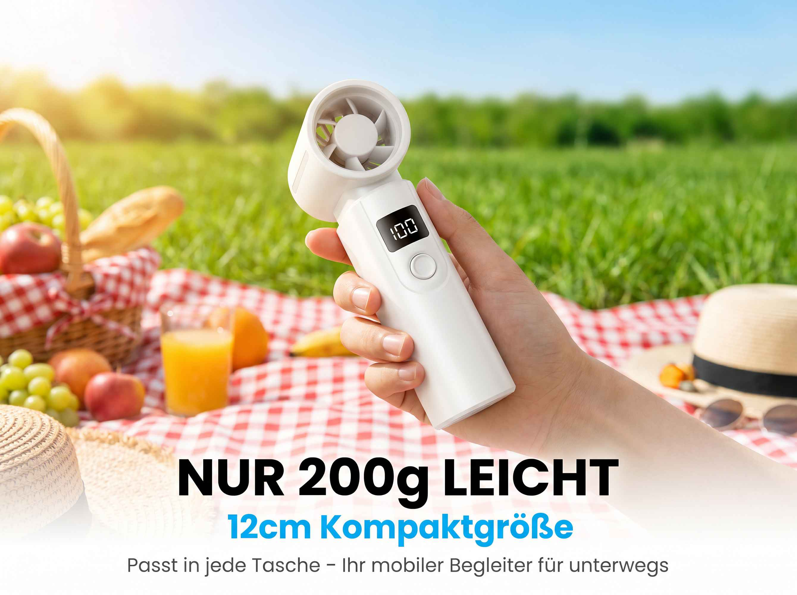Eine Hand hält einen weißen Ventilator mit Display im Freien bei einem Picknick.