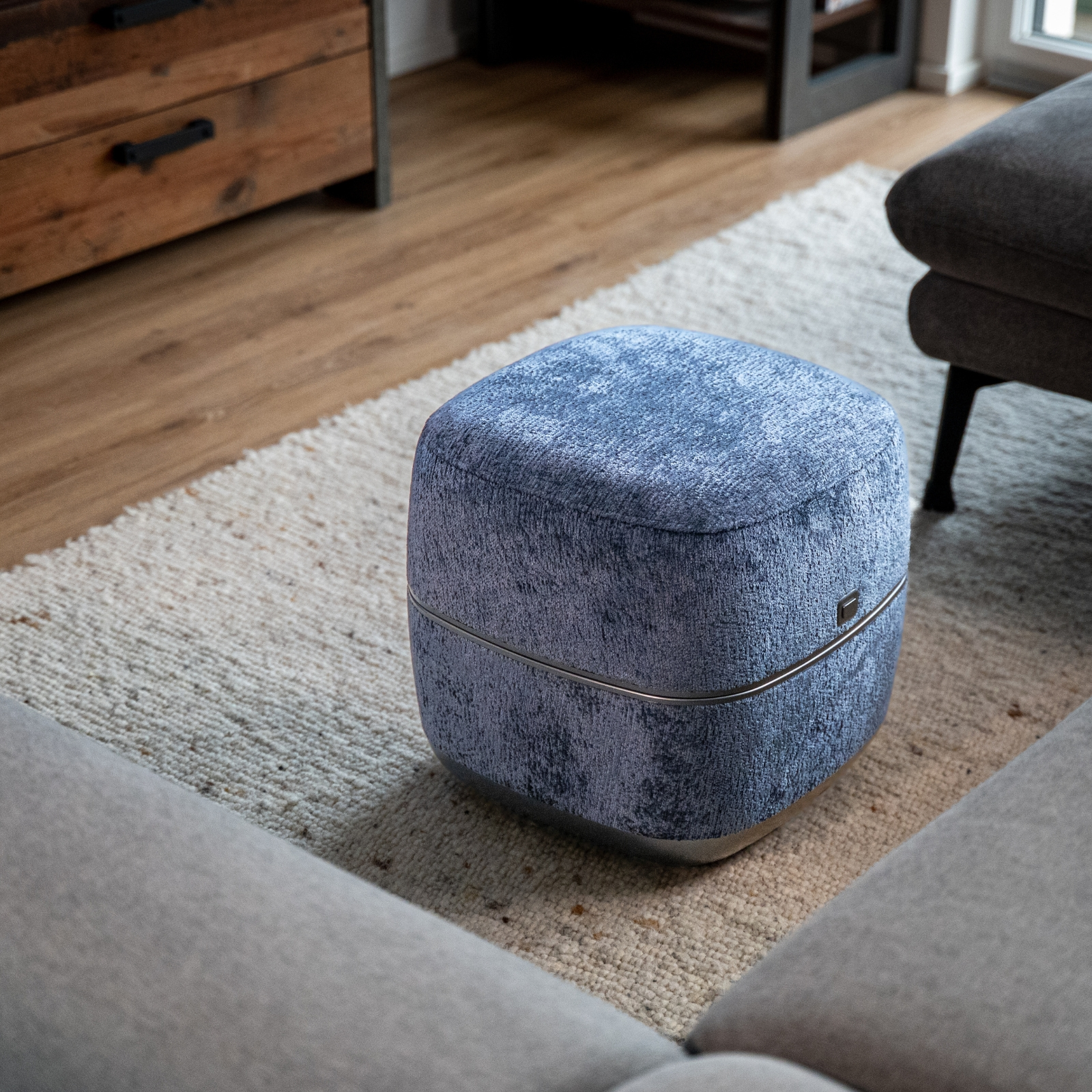 Ein blauer Hocker steht auf einem Teppich neben einem Sofa.