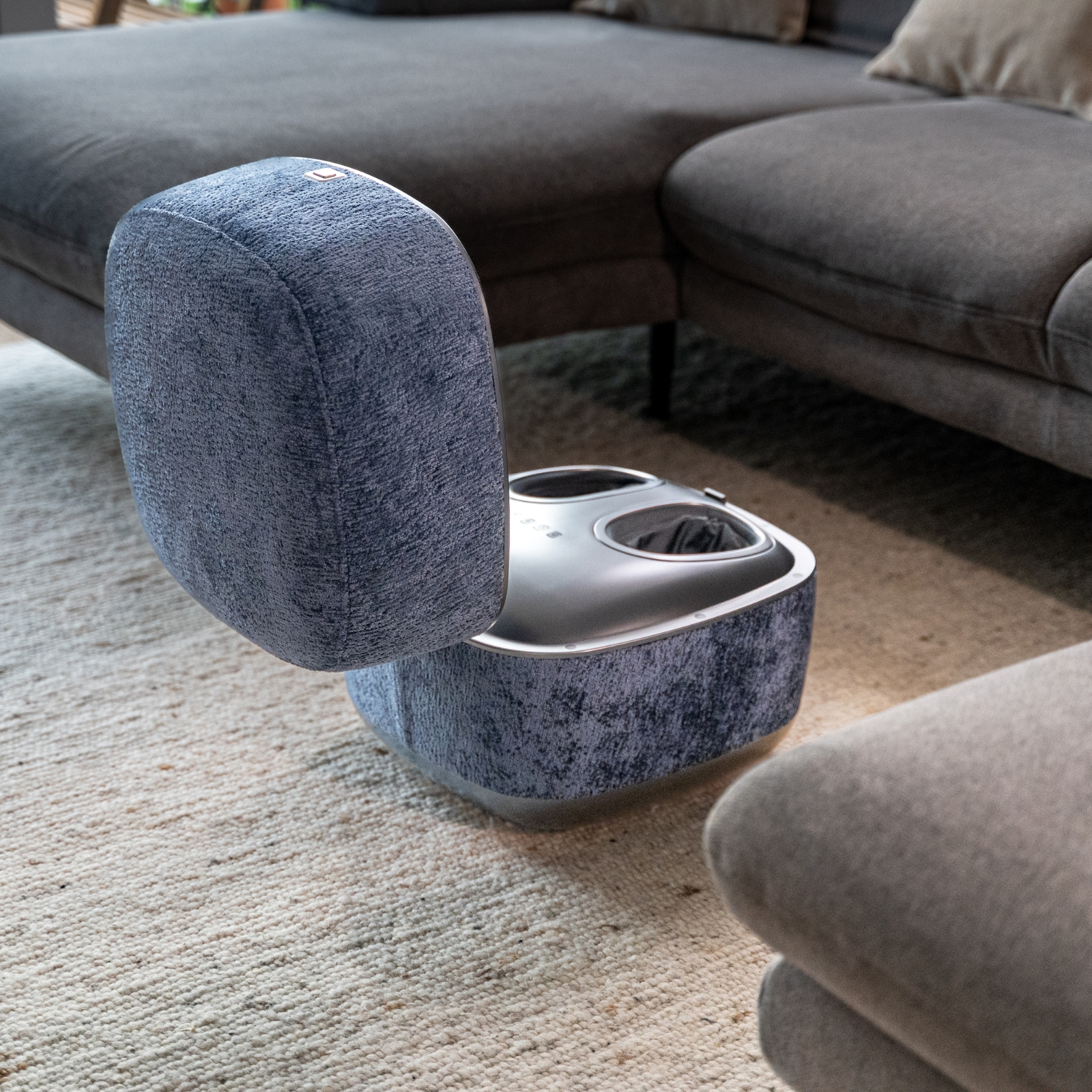 Ein blauer Fußmassagegerät steht auf einem Teppich vor einem Sofa.
