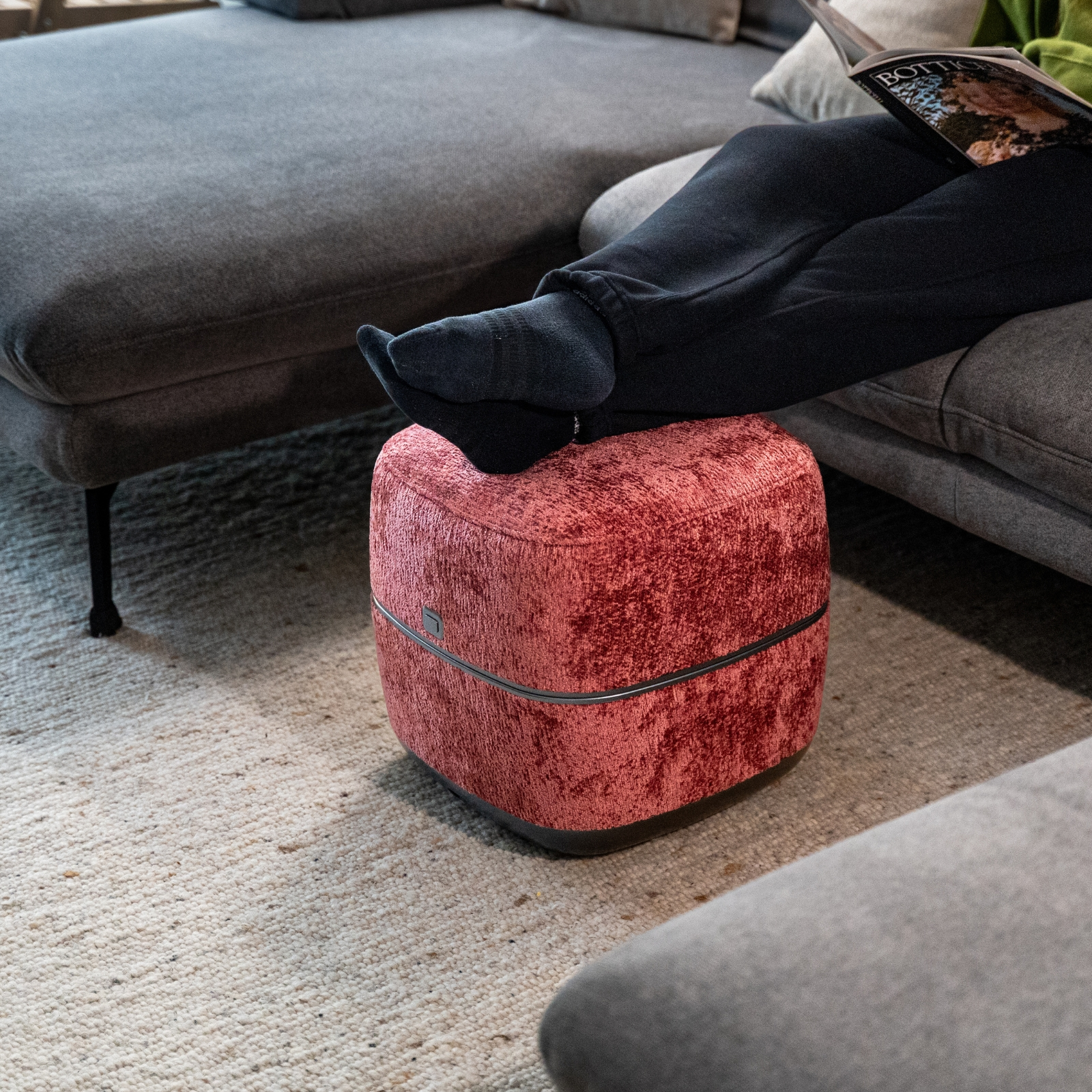 Person mit schwarzen Socken ruht Füße auf rotem Hocker neben Sofa.