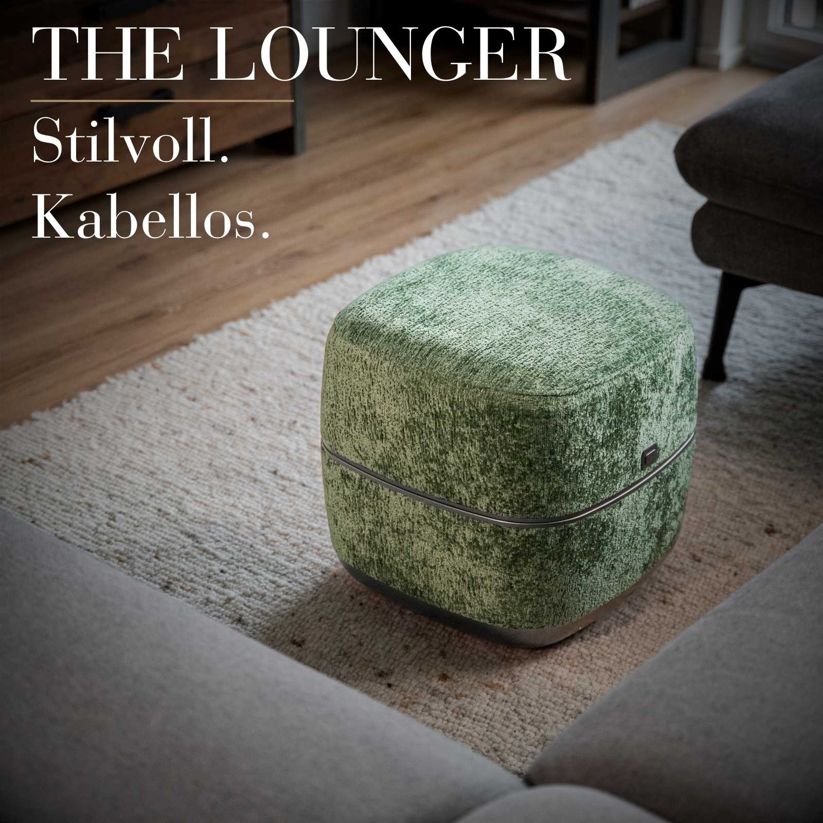 Ein grüner Hocker mit Samtbezug steht auf einem Teppich neben einem Sofa.