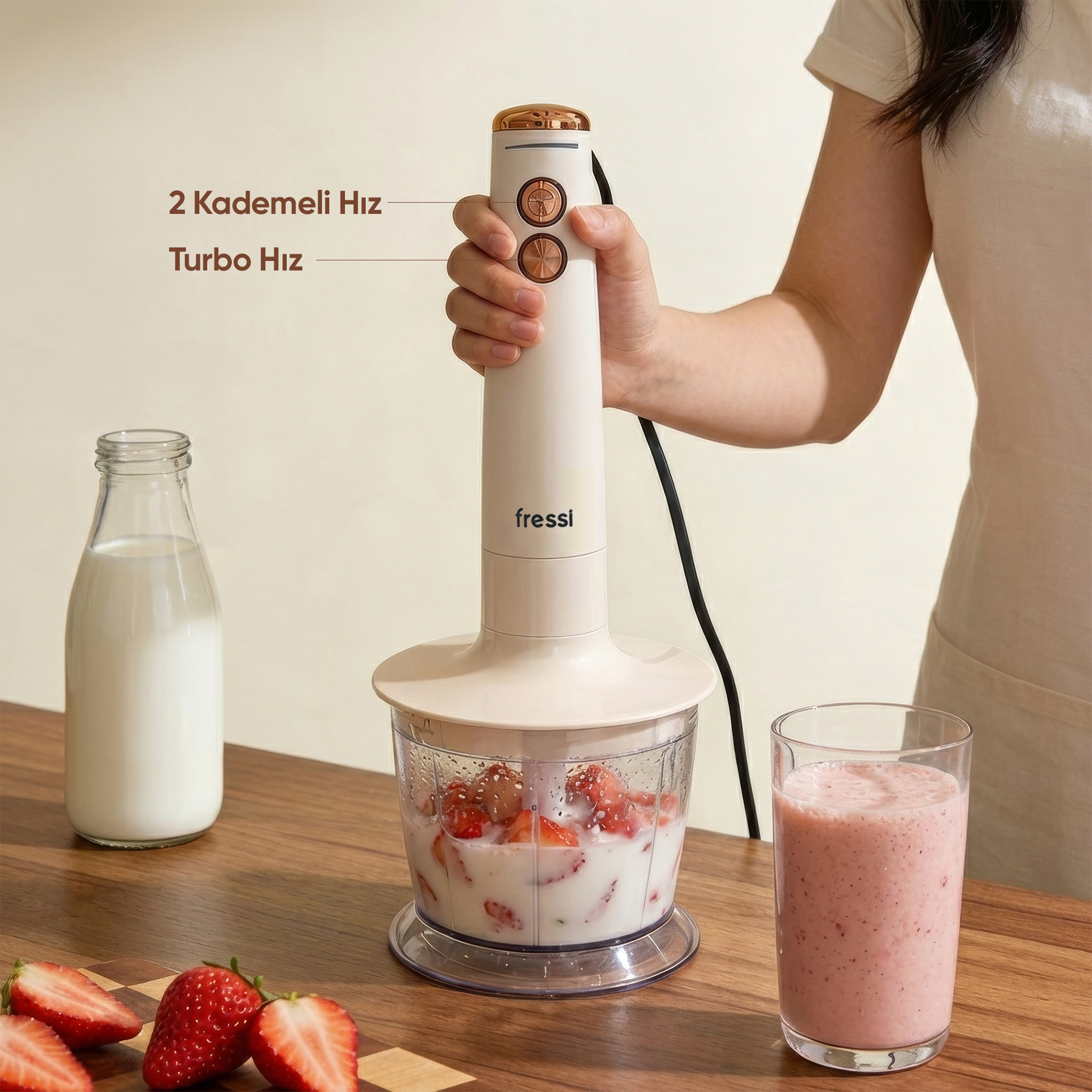 Çilek ve süt dolu haznenin üzerindeki el blenderı, yanında süt şişesi ve smoothie bardağı.