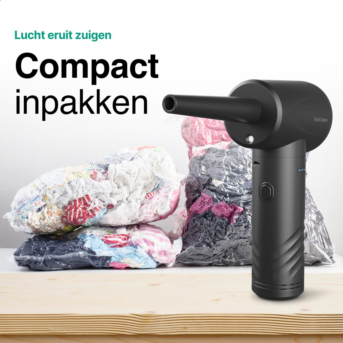 Zwarte vacuümsealer naast samengeperste kledingzakken op houten tafel.