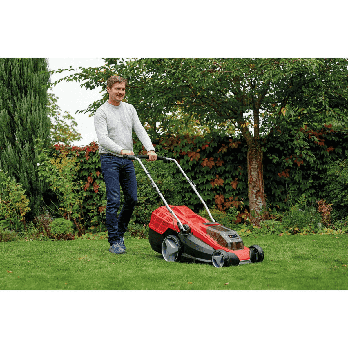 Ein Mann schiebt einen roten Rasenmäher durch einen gepflegten Garten.