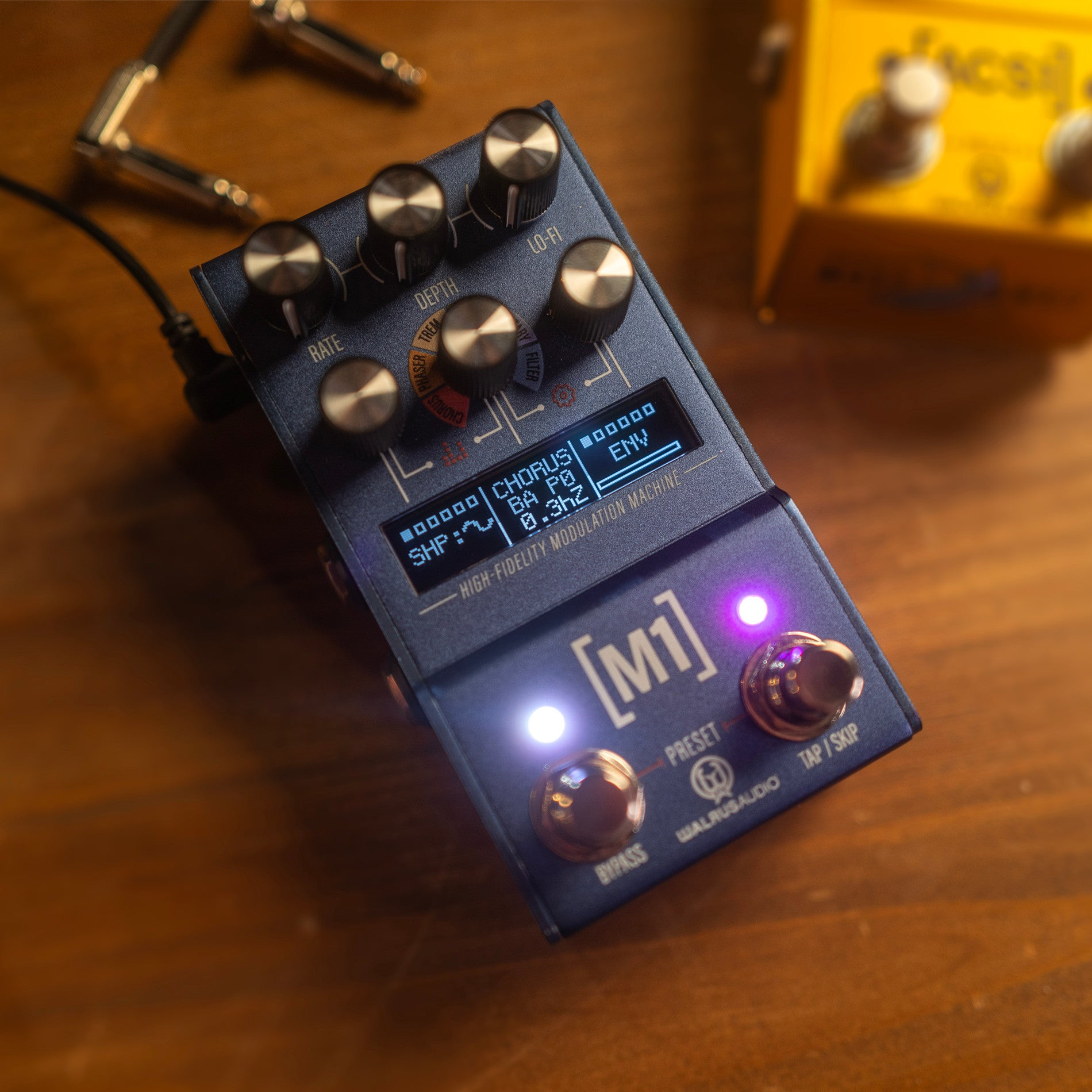 A blue Walrus Audio M1 modulation pedal with knobs, a screen, and illuminated buttons on a wooden surface.