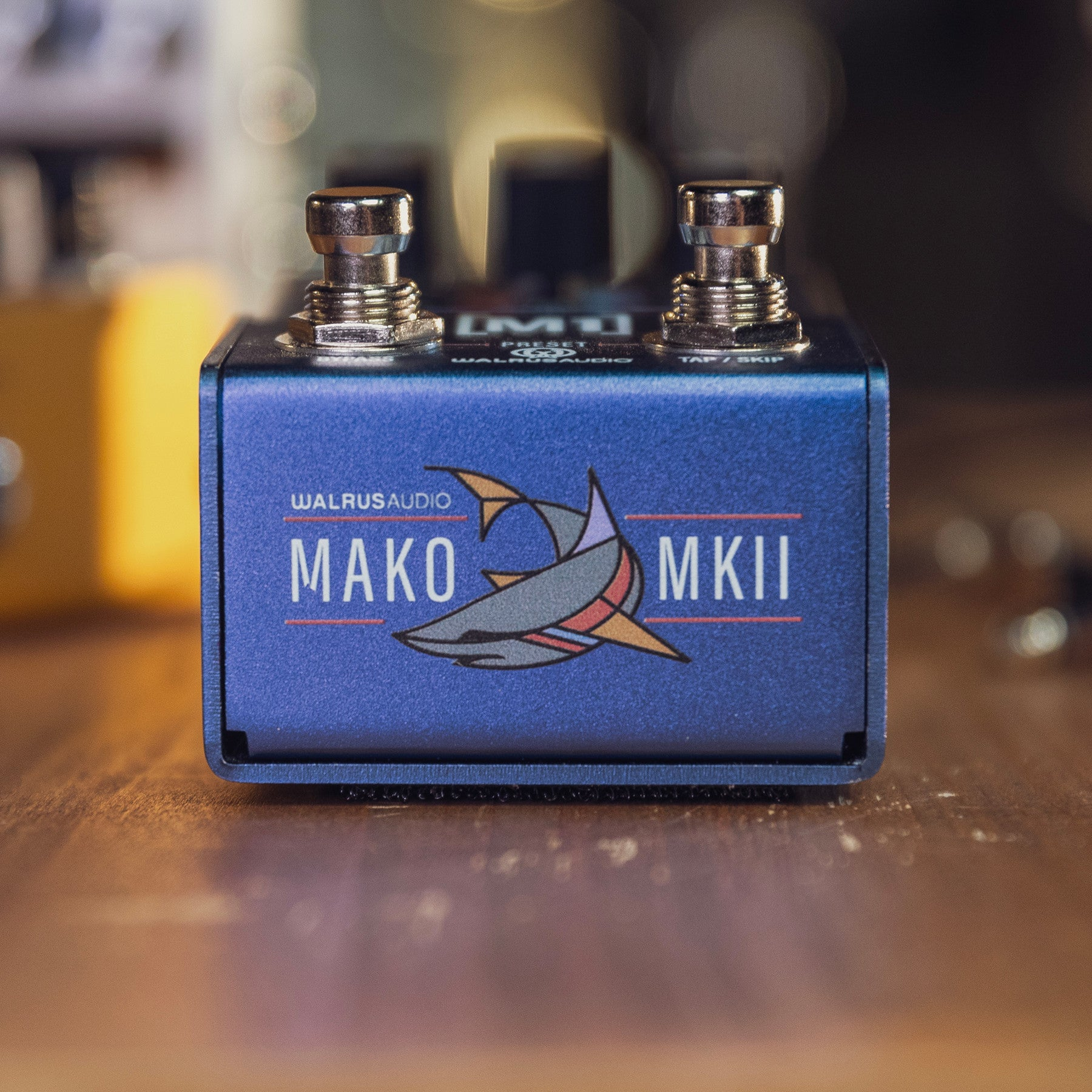 Blue effect pedal with shark logo and two silver footswitches on a wooden table.