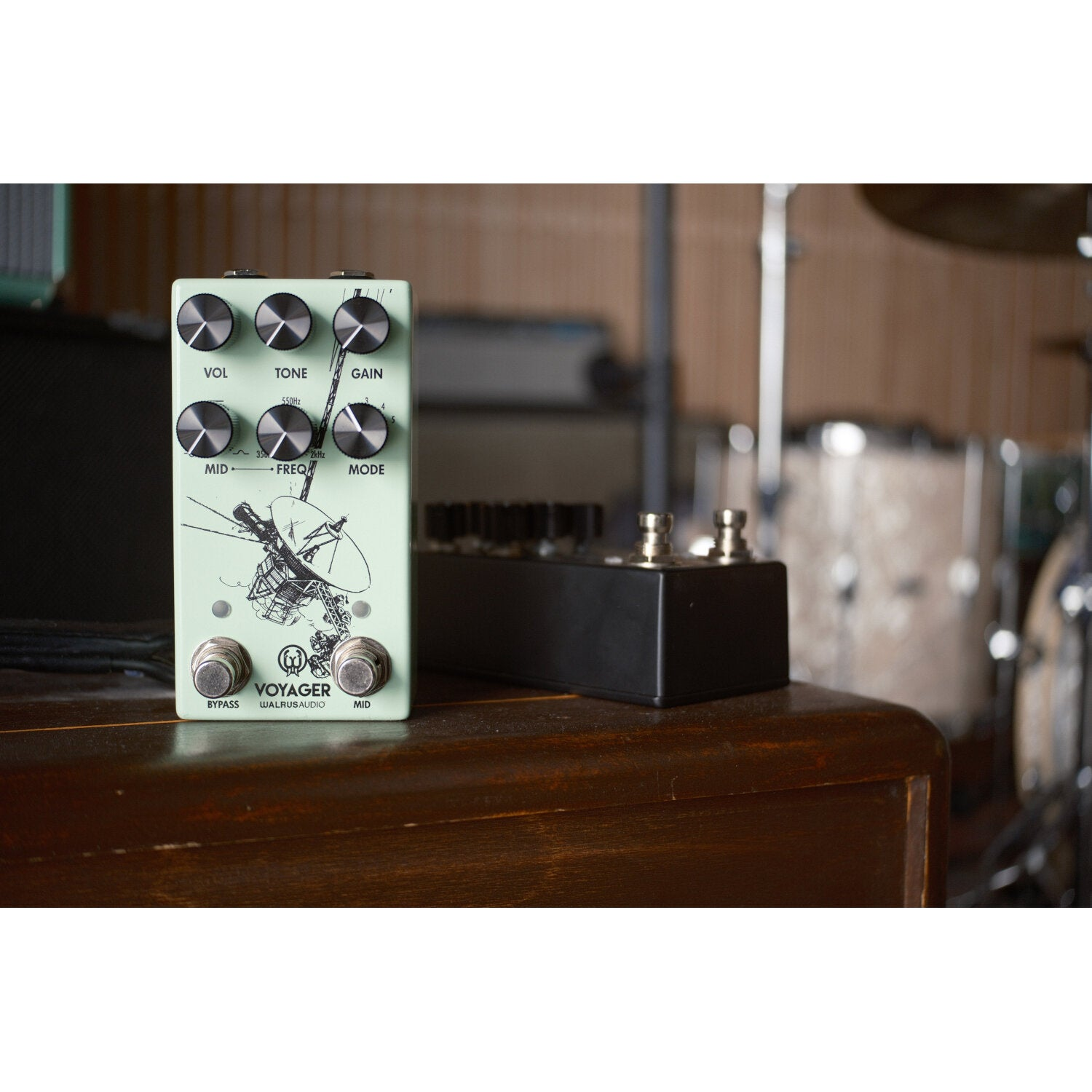 A mint green guitar pedal with knobs and graphics sits on a wooden surface.