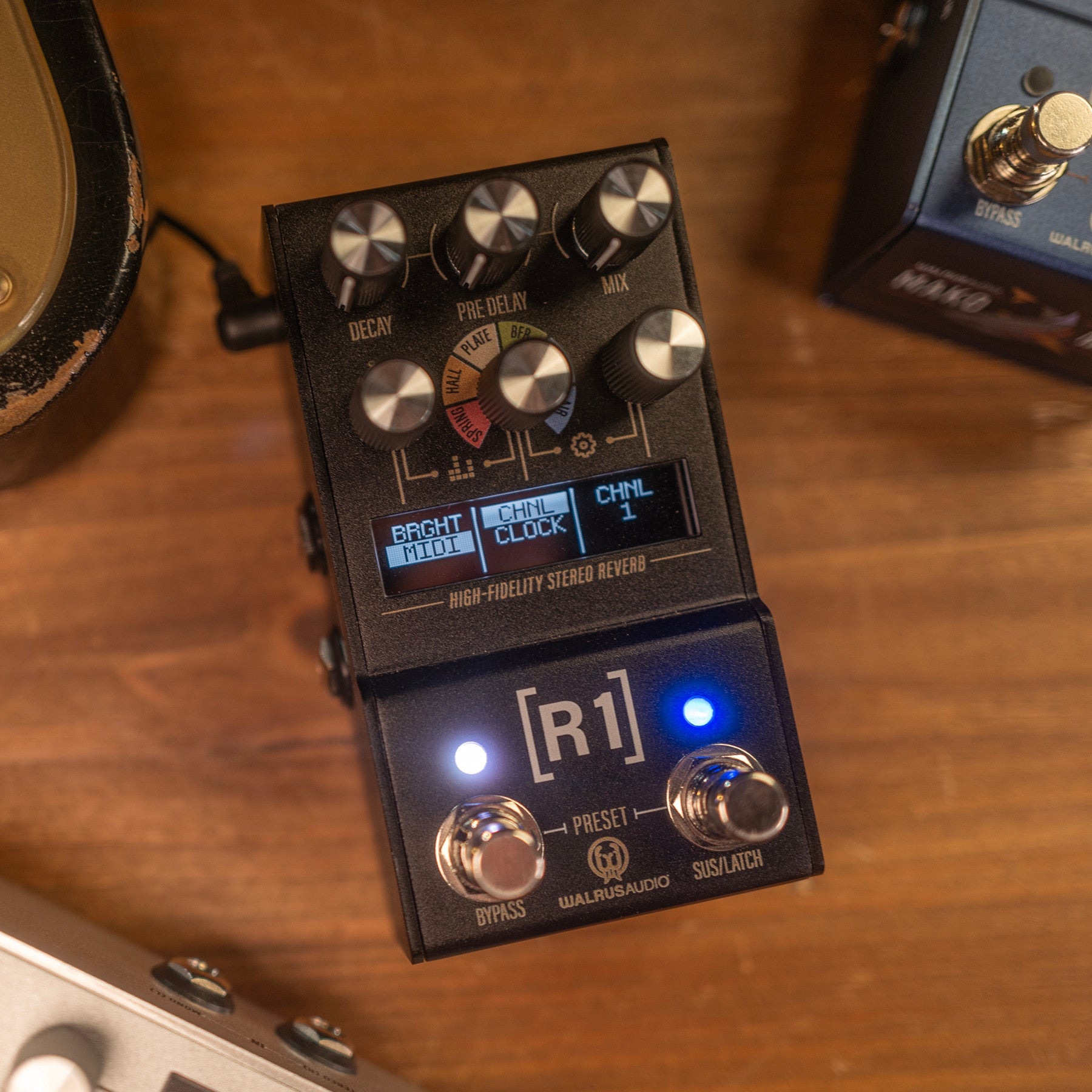 A black guitar effects pedal with knobs and a display on a wooden table.