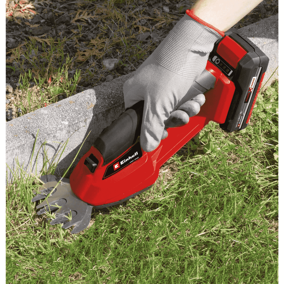 Eine Hand mit Handschuh benutzt einen roten Akku-Rasentrimmer am Rasenrand.