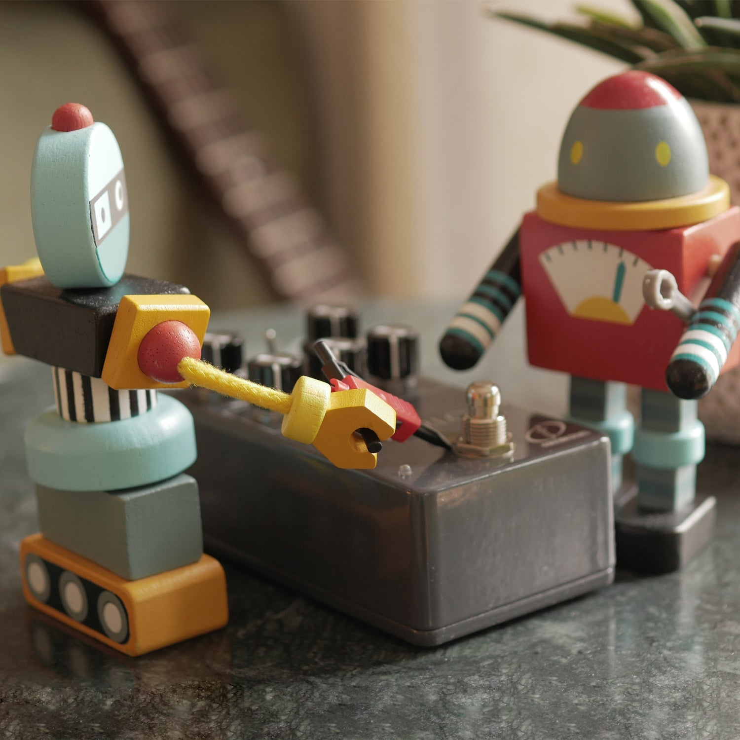Two wooden robots stand before an effect pedal on a marble table.