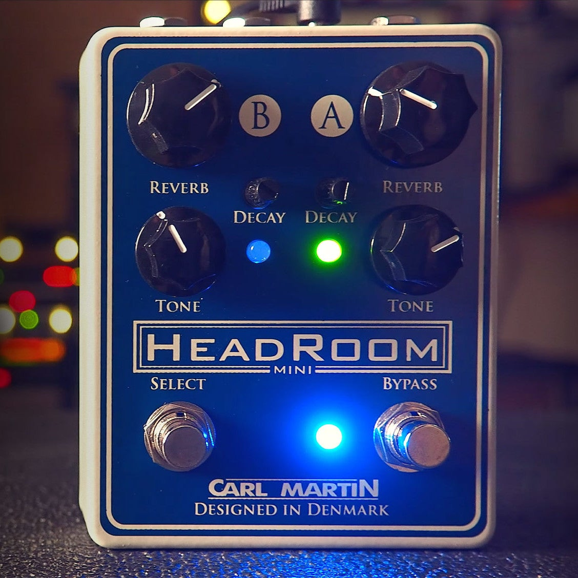 A blue guitar effects pedal with white text and knobs. Lights are on.