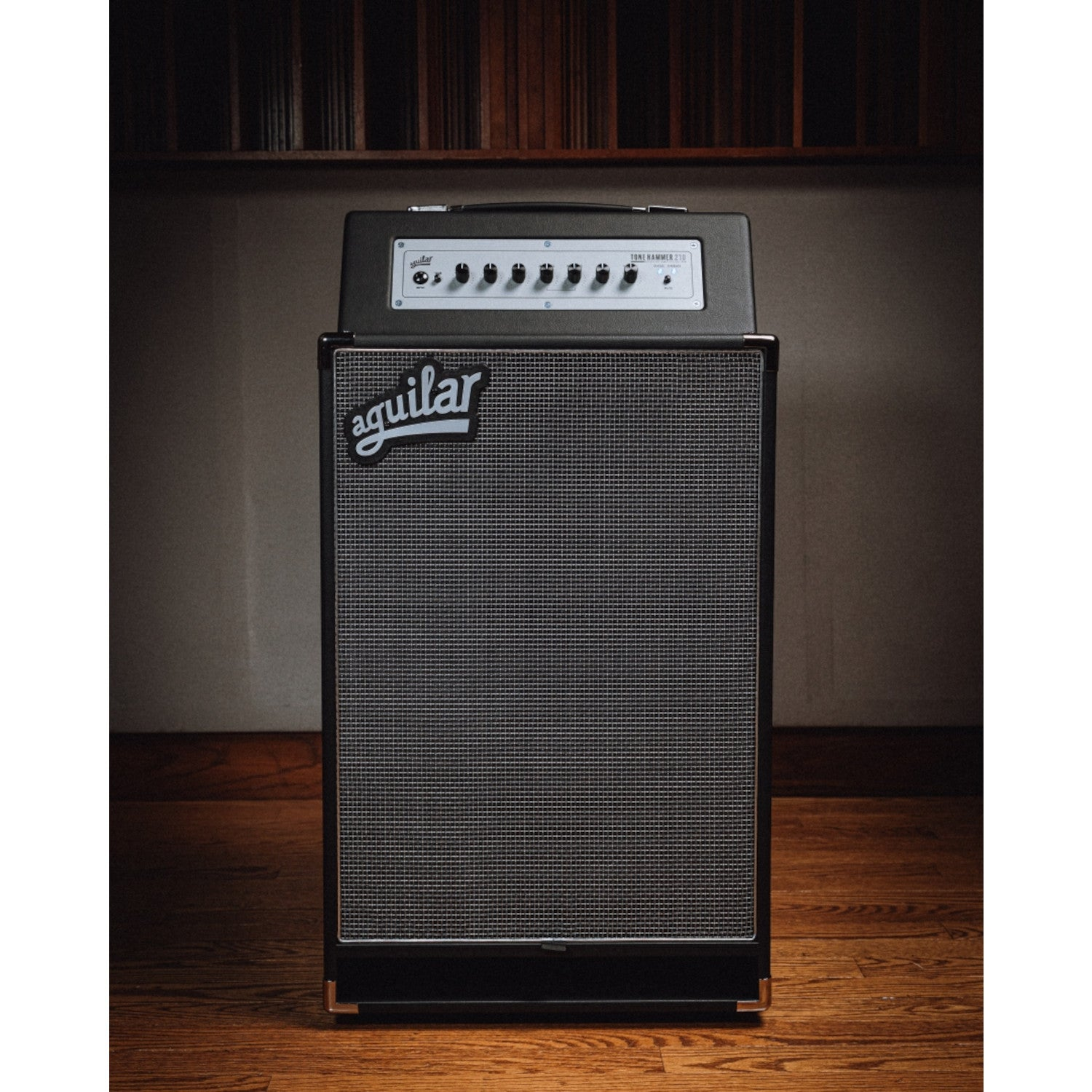Een zwarte Aguilar basversterker met zilveren speakergrill staat op een houten vloer.
