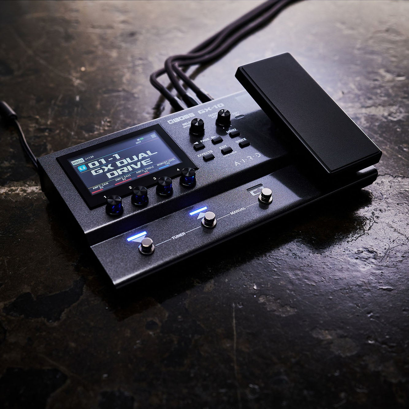 A dark, textured surface with a black BOSS GX-10 multi-effects guitar pedal and expression pedal.