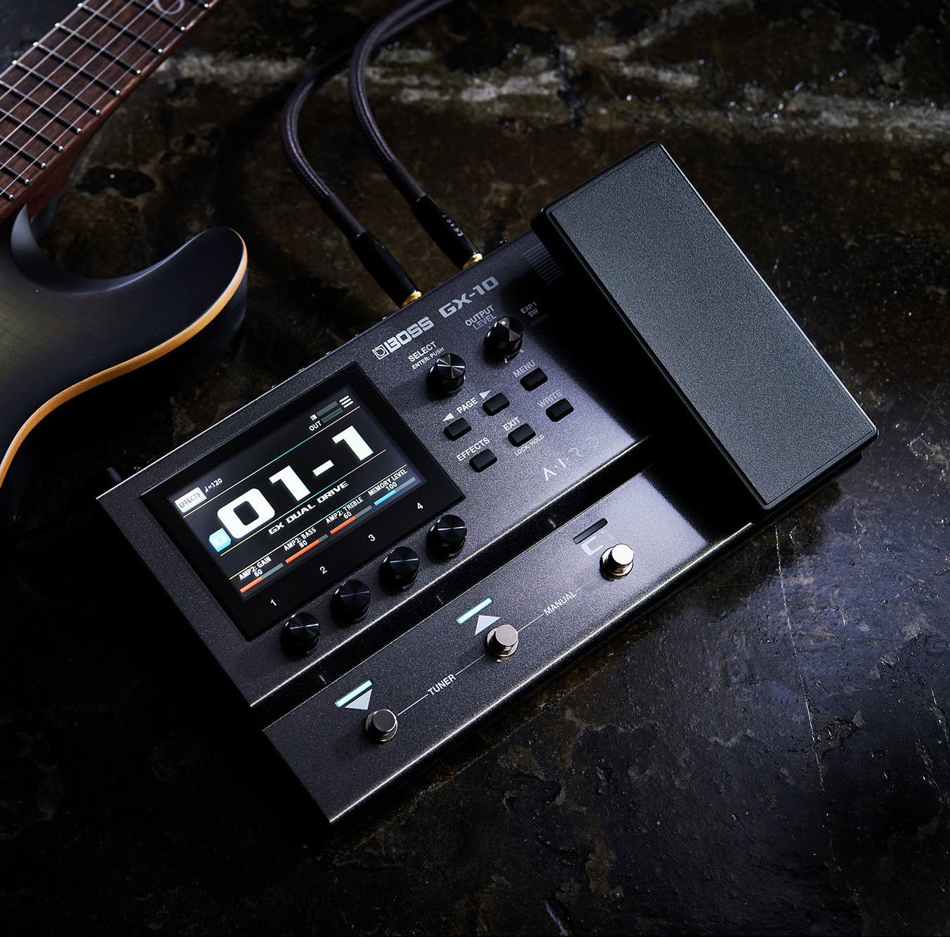 A black electric guitar multi-effects processor with display, pedals, and cables, next to a guitar.