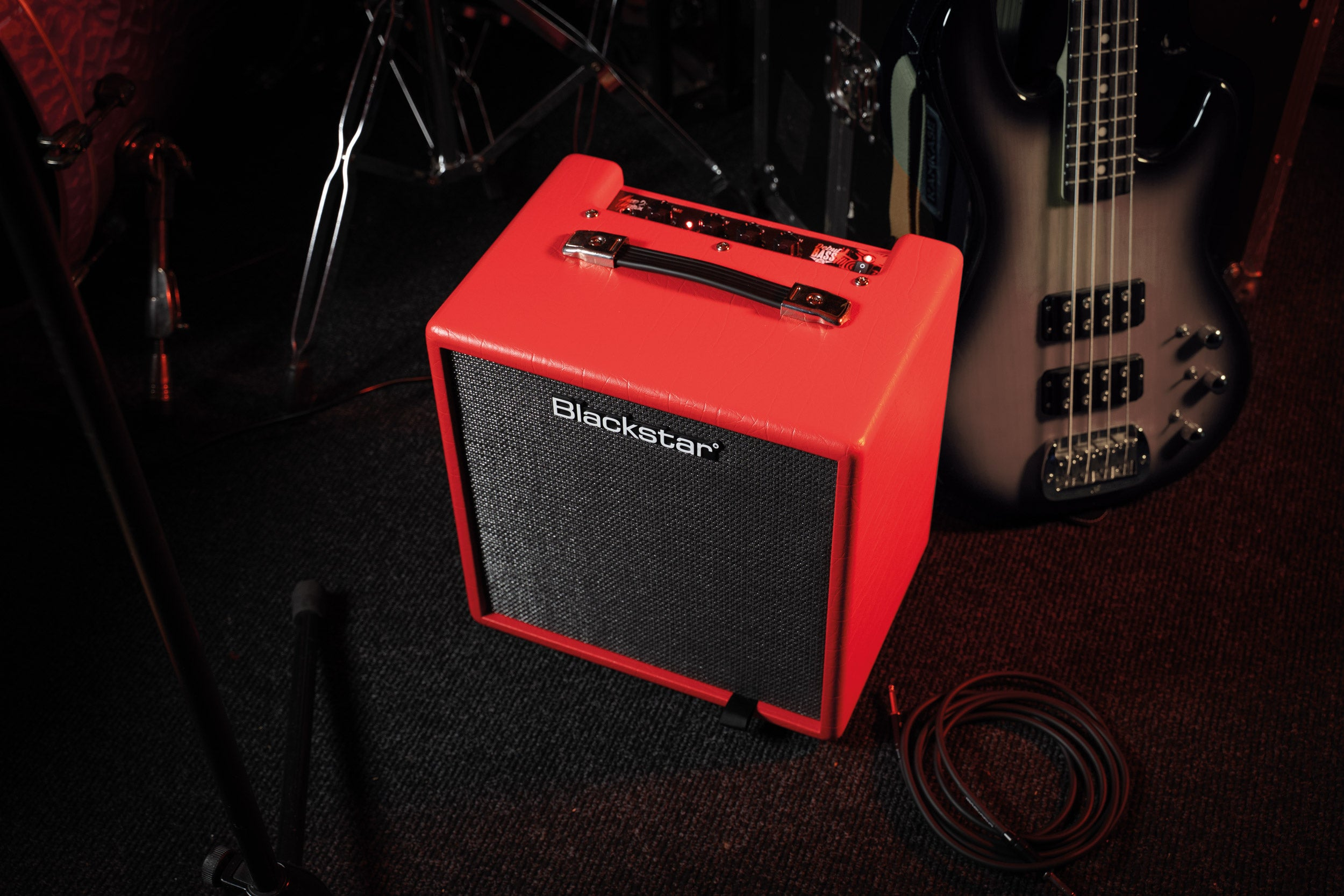 A red guitar amplifier is placed next to a bass and drum kit pieces.