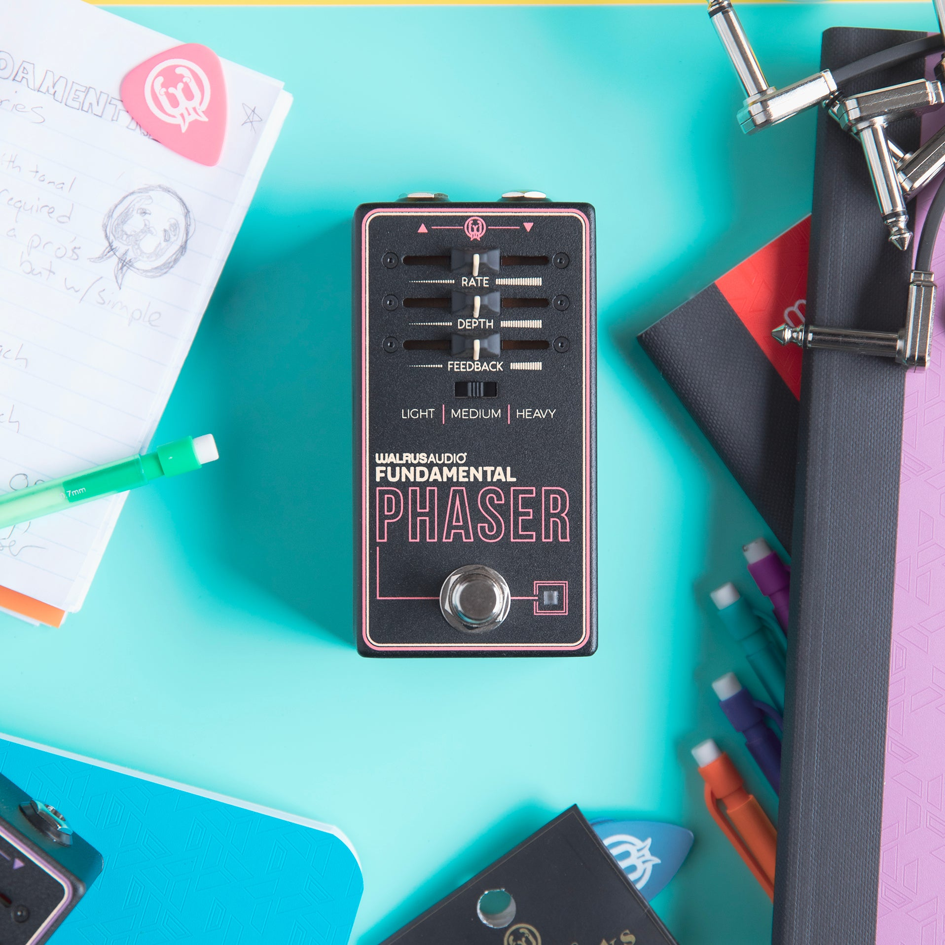 A Walrus Audio Phaser pedal lies on a teal desk, surrounded by notebooks and cables.