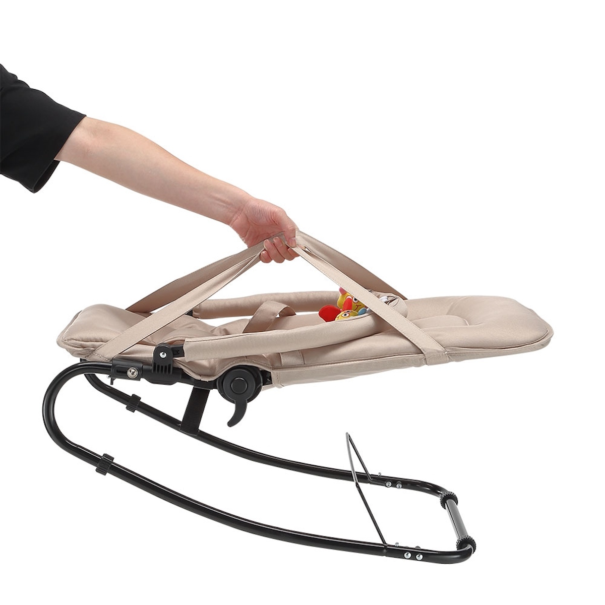 Eine Hand hält den Gurt einer zusammengeklappten beige Babywippe mit Spielzeug.