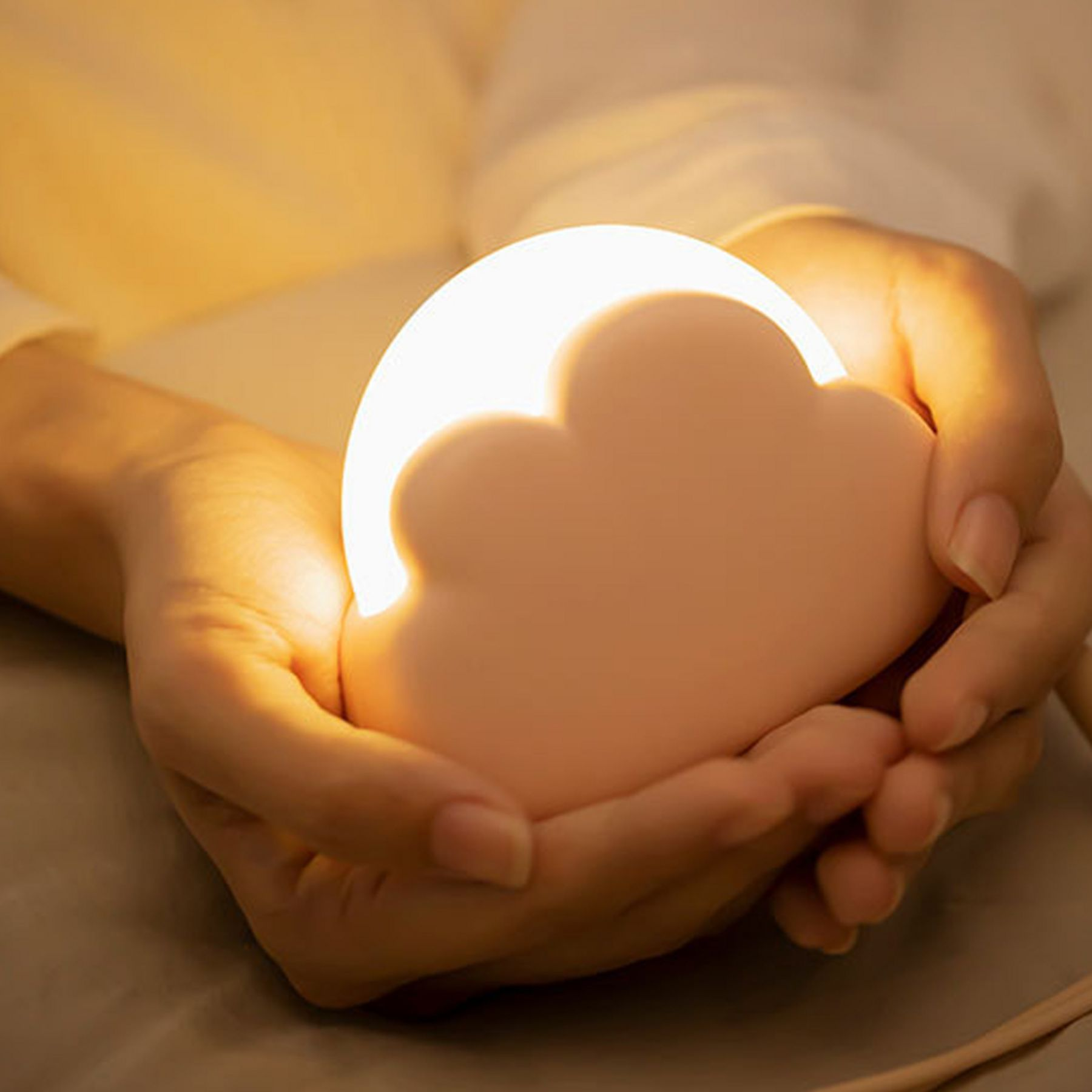 Hände halten eine leuchtende, wolkenförmige Lampe.