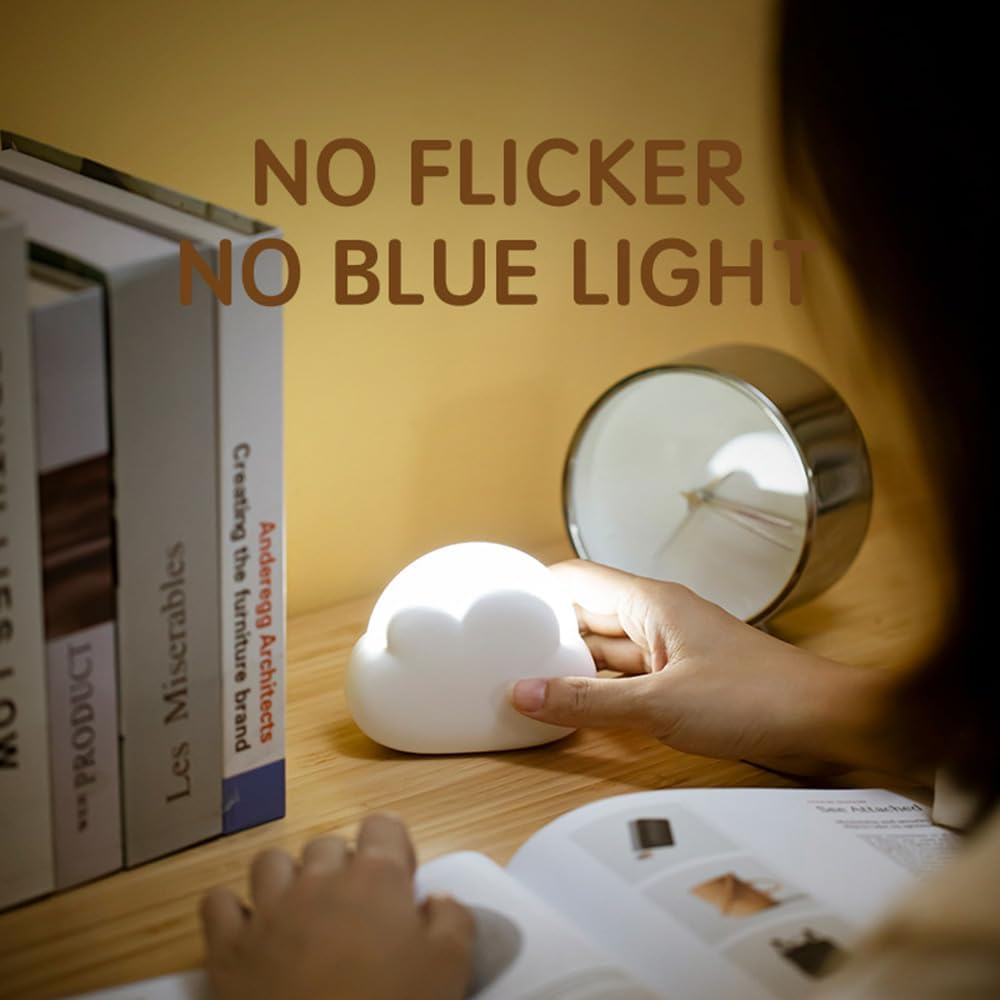 Eine Hand berührt eine weiße Wolkenlampe auf einem Schreibtisch neben Büchern und einem Wecker.