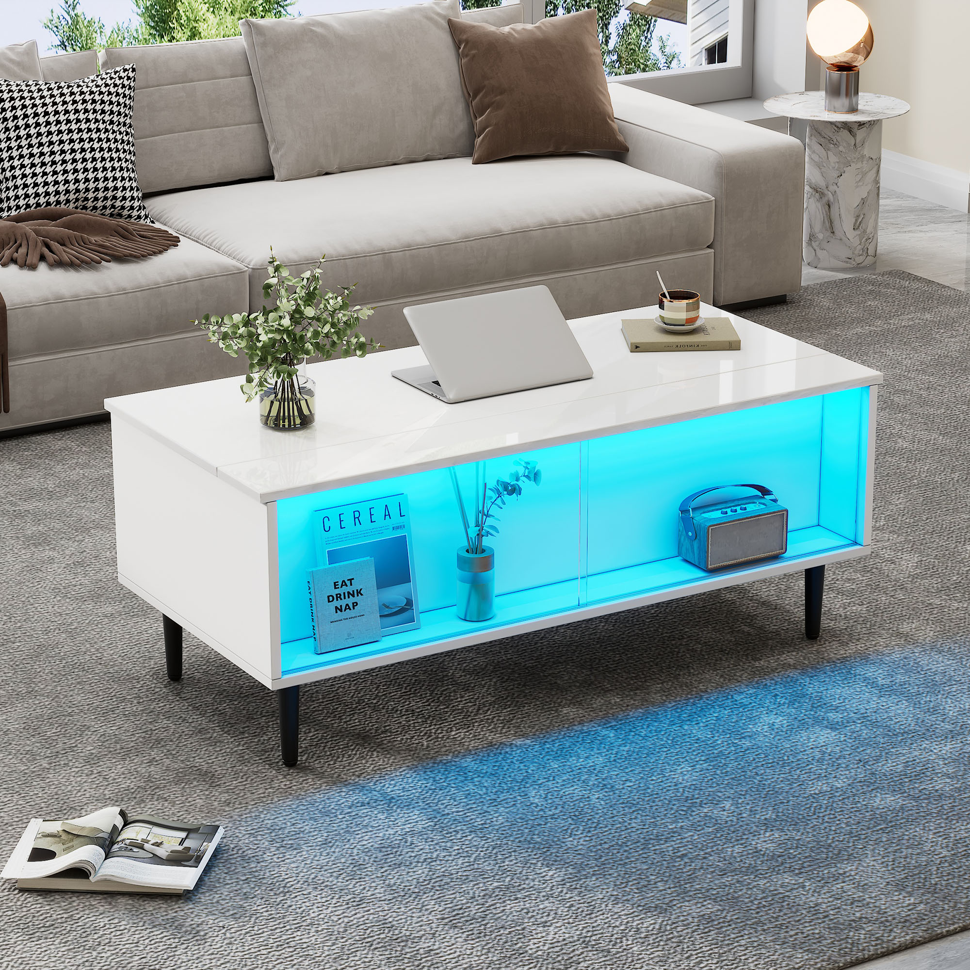 Ein weißer Couchtisch mit blauer LED-Beleuchtung, Laptop, Büchern und Radio.
